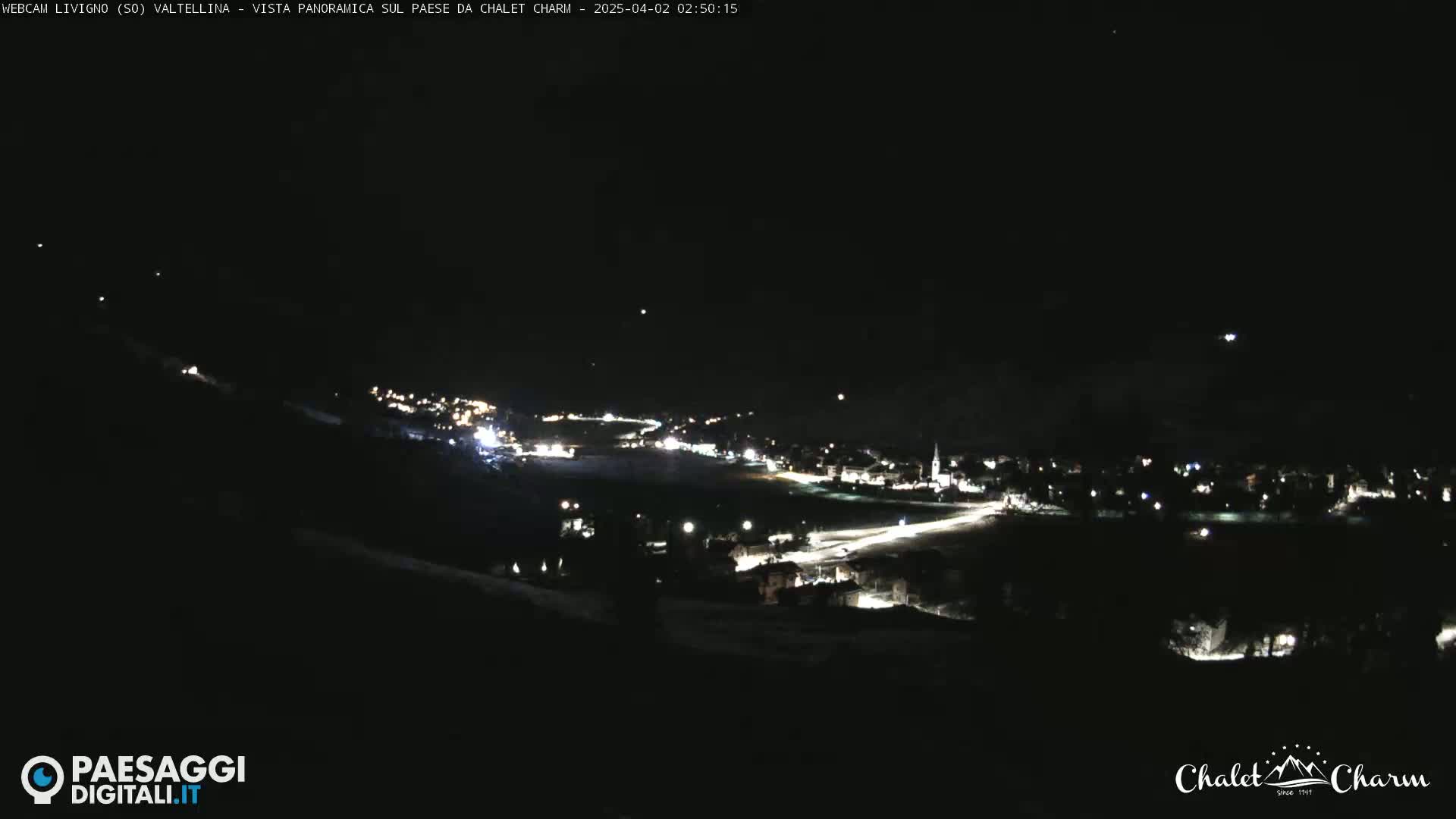 A nighttime panoramic view of a town illuminated by streetlights, under a clear, dark sky.