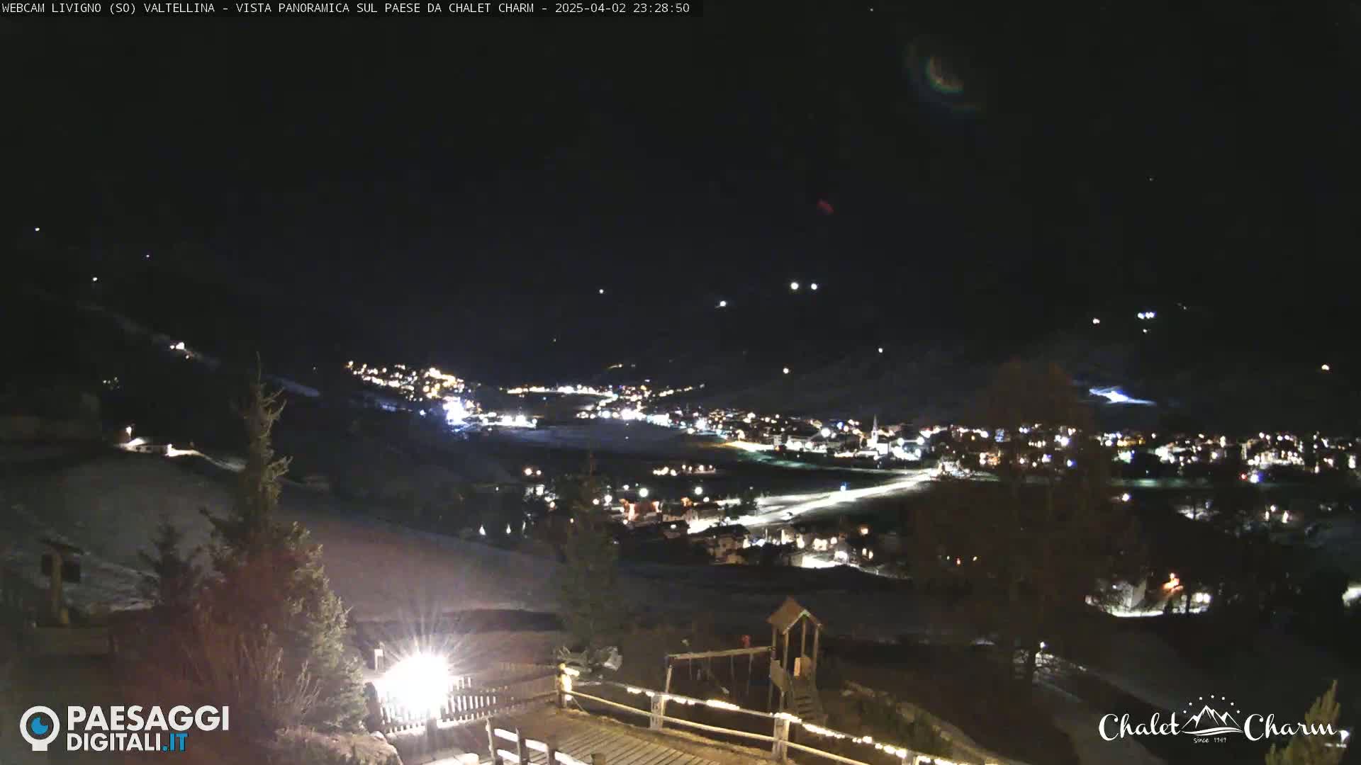 A nighttime panoramic view of a snow-covered town illuminated by lights, seen from a higher vantage point under a clear, starry sky.