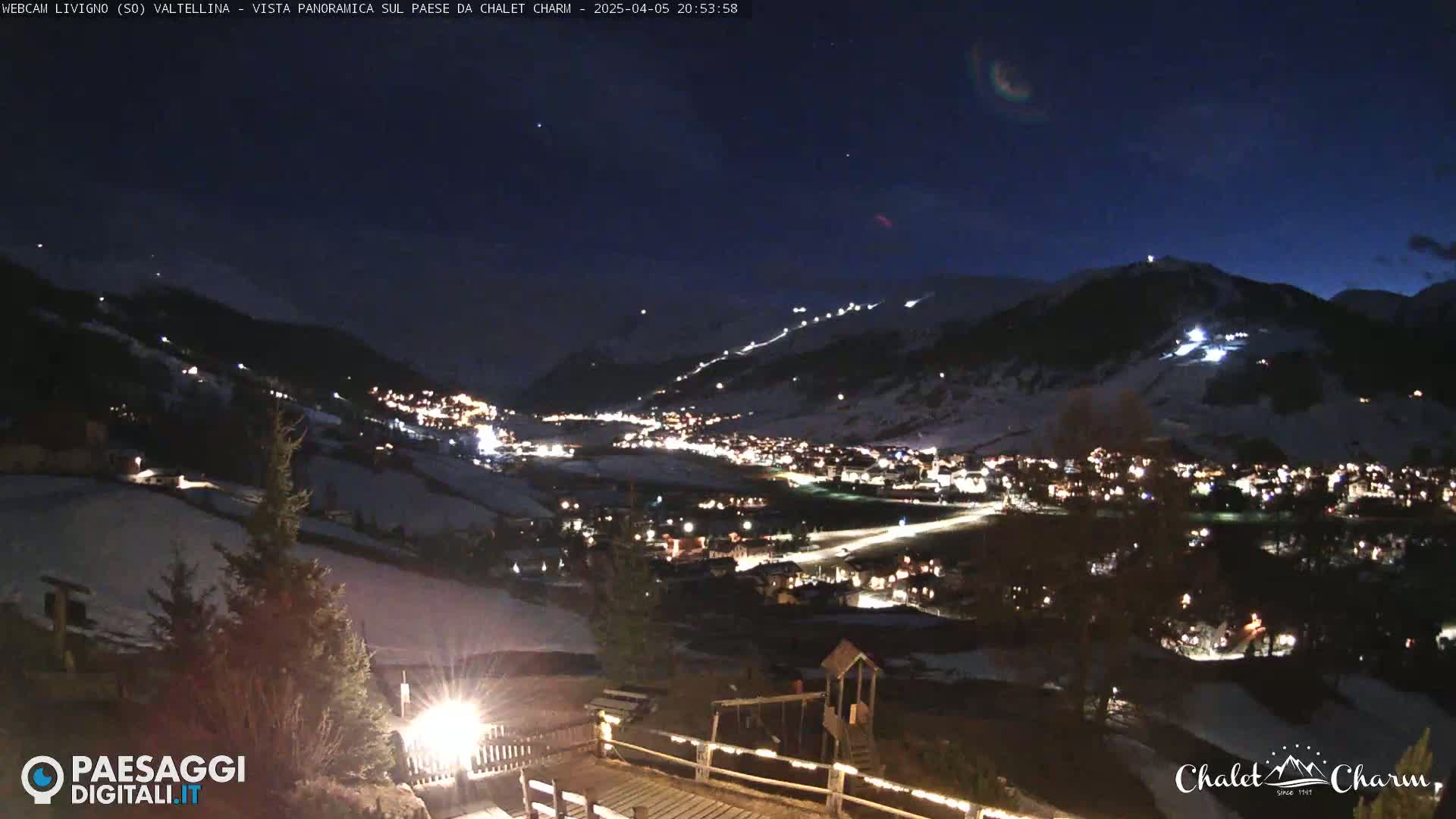 A nighttime, panoramic view of a snow-covered village nestled in a valley under a dark, starry sky.