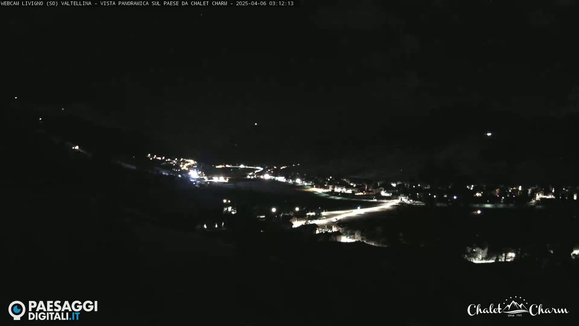 A nighttime, panoramic view of a small town illuminated by scattered lights under a dark sky.