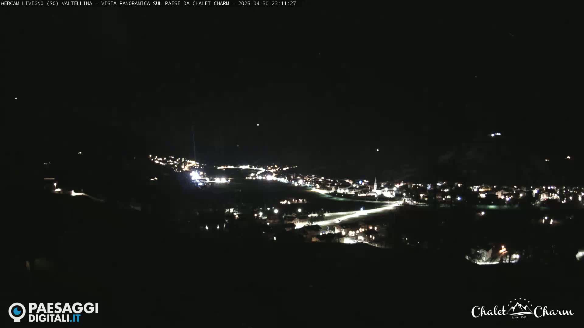 A nighttime, panoramic view of a village illuminated by lights under a clear, dark sky.