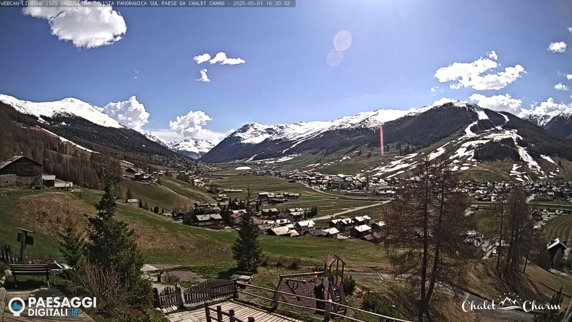 A sunny day reveals a snow-capped mountain range overlooking a valley town with a playground in the foreground.