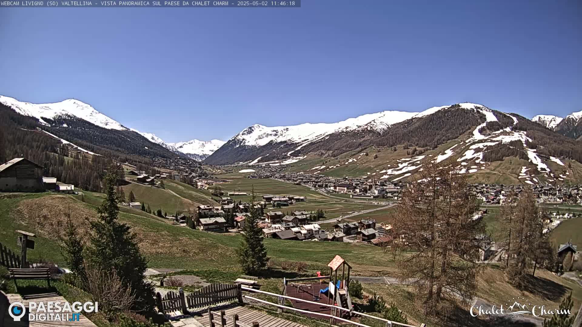 A sunny view overlooking a village nestled in a valley between snow-capped mountains.
