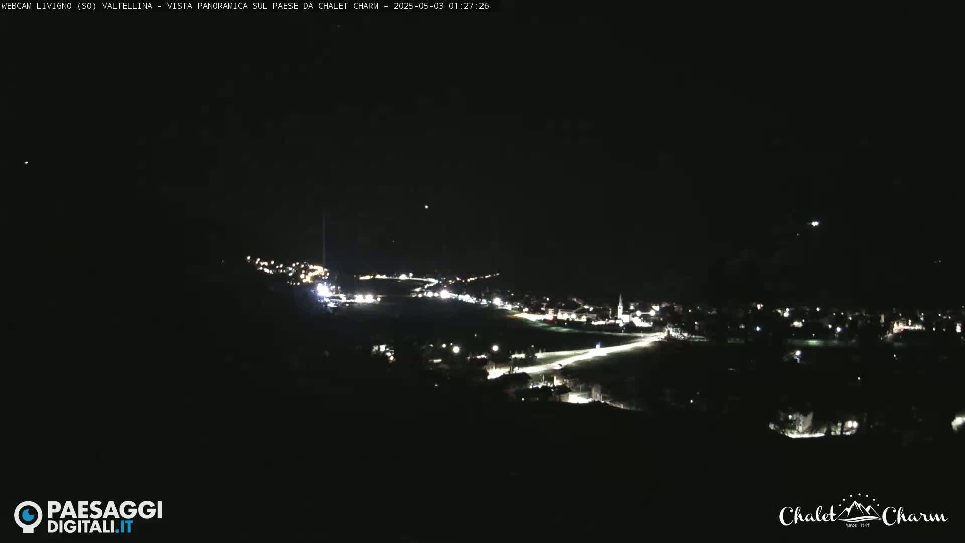 A nighttime panoramic view of a town illuminated by scattered lights under a clear, dark sky.