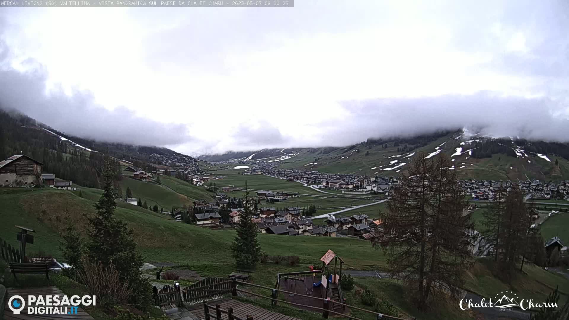 A valley town nestled in a mountainous region is partly obscured by low-hanging clouds on an overcast day.