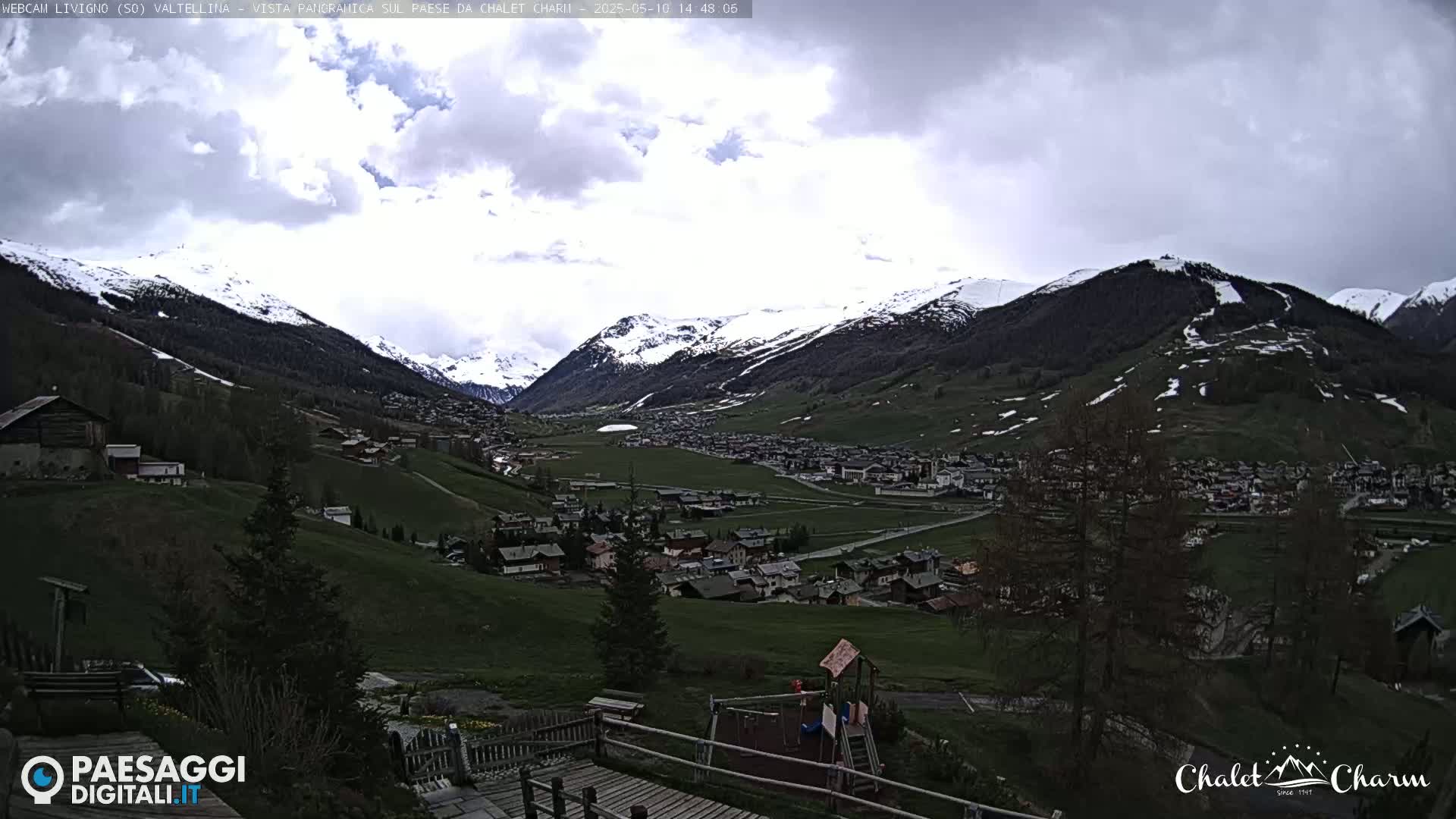 A mountain valley town with snow-capped mountains in the background under a cloudy sky.