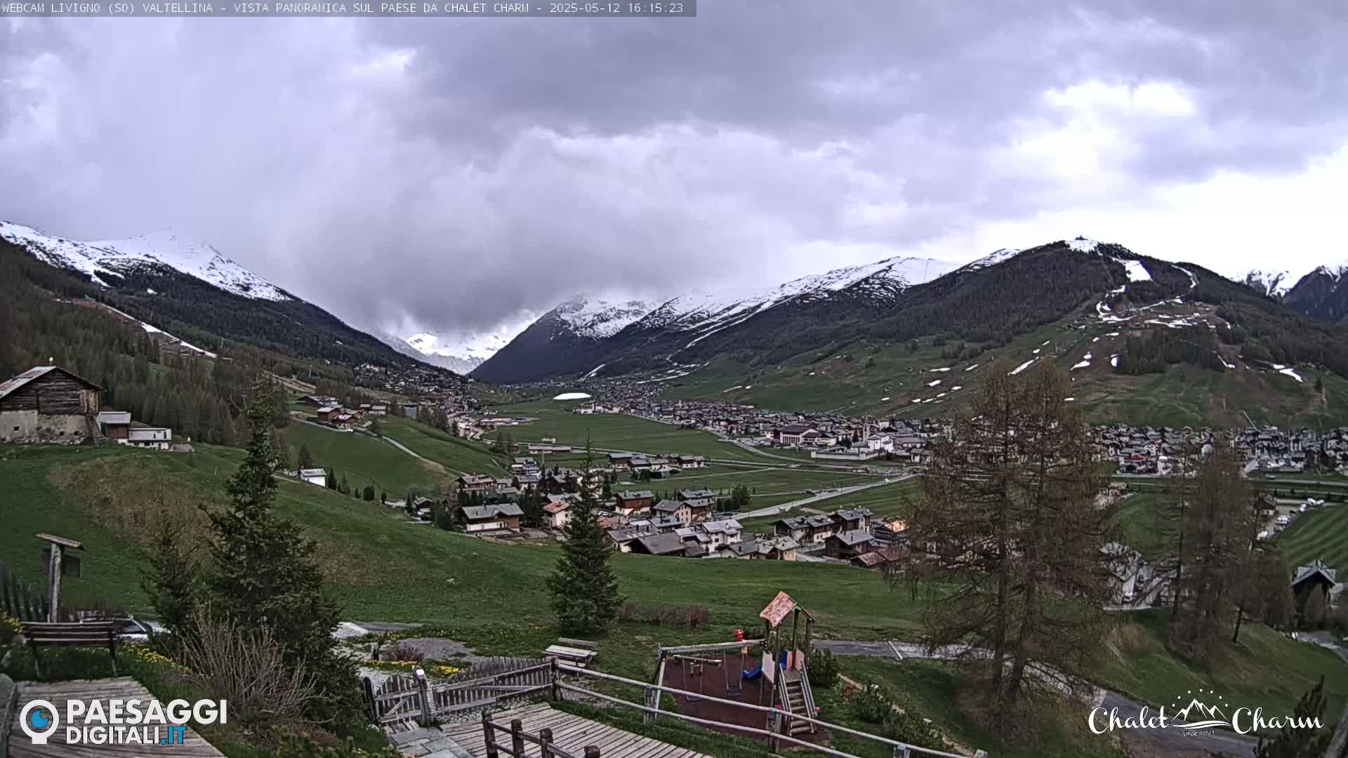 A panoramic view of a snow-capped mountain range and a village nestled in a valley under a cloudy sky.
