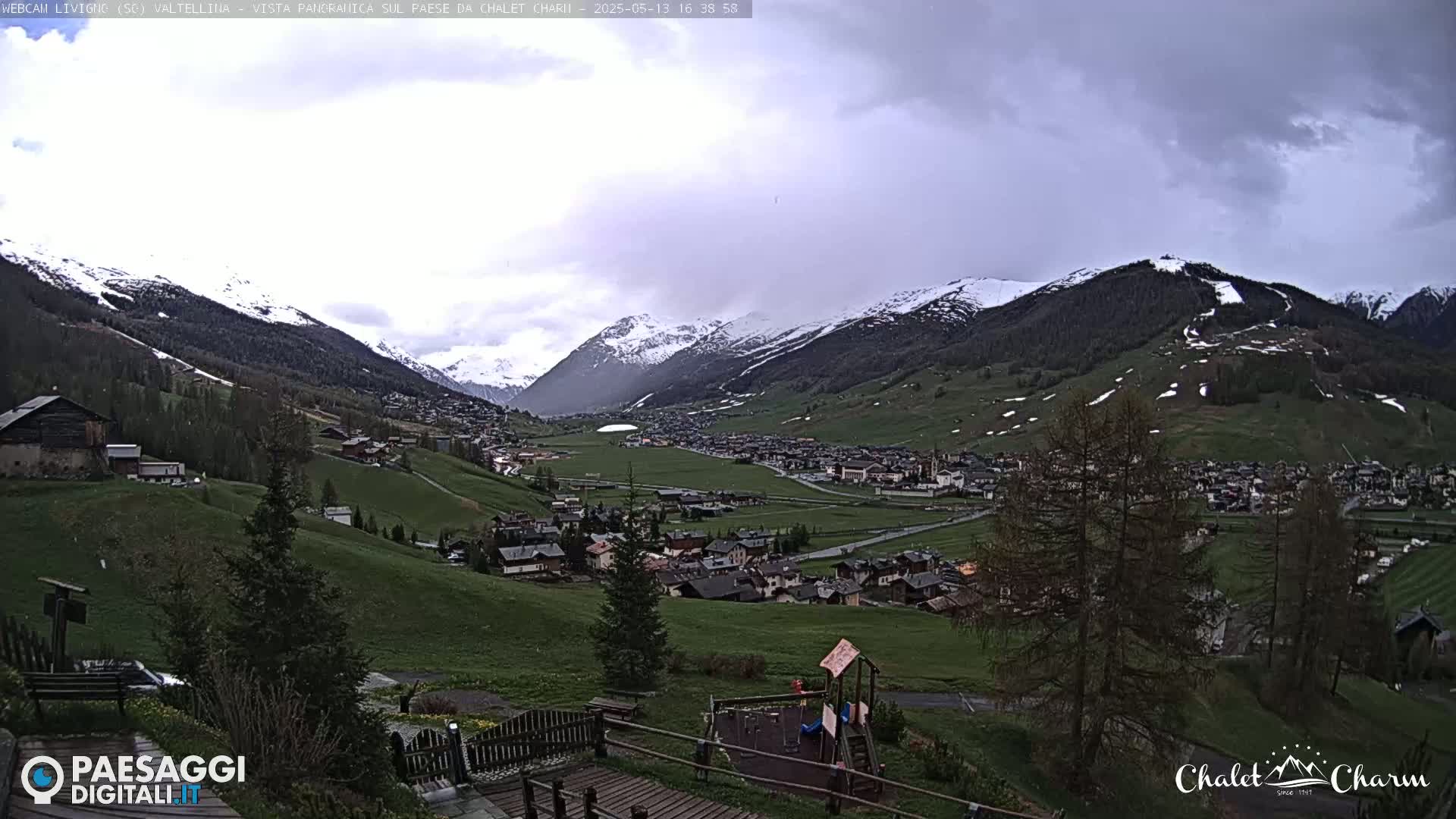 A panoramic view of a snow-capped mountain valley town under an overcast sky.