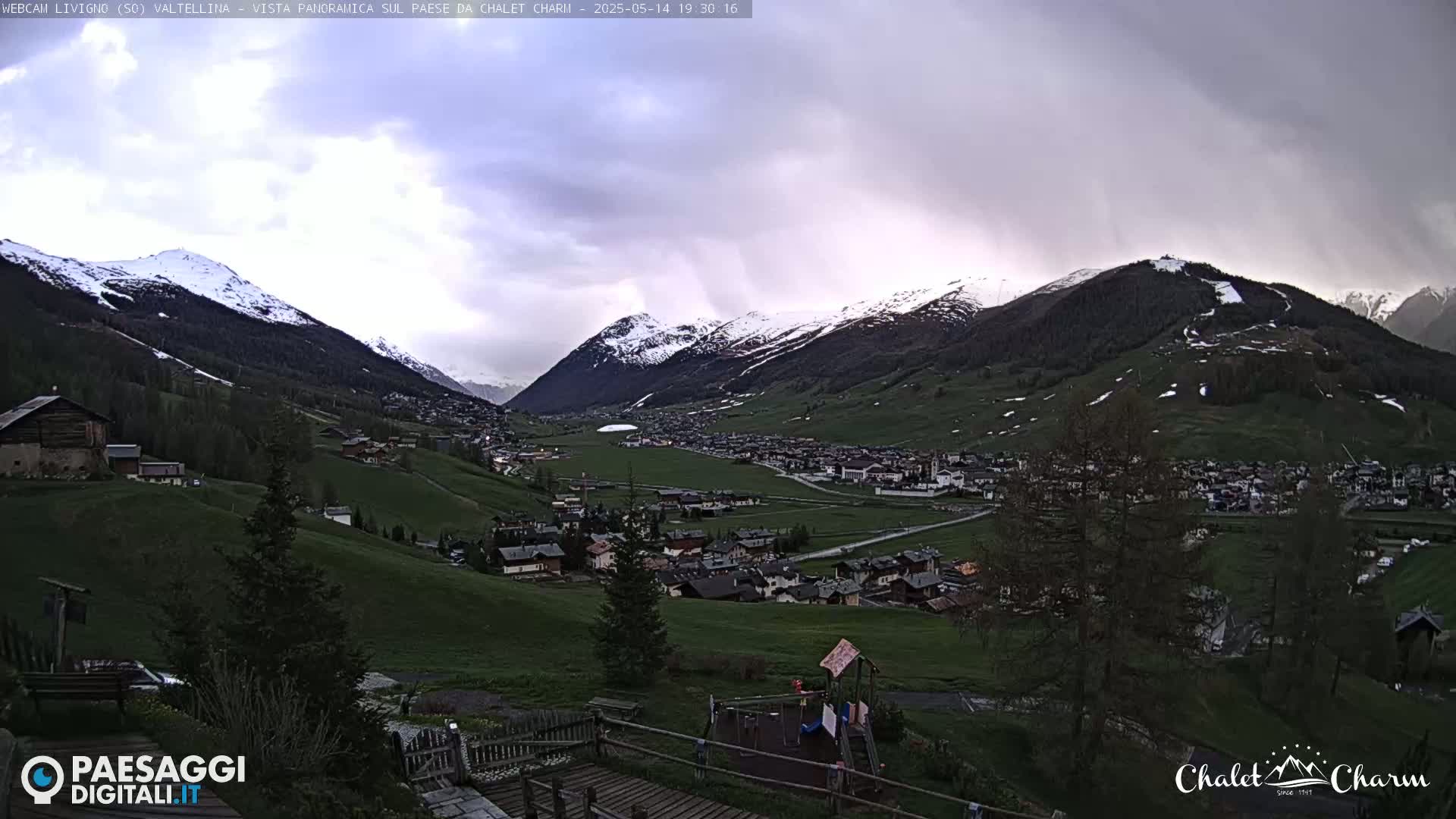A panoramic view of a snow-capped mountain valley village under an overcast sky.
