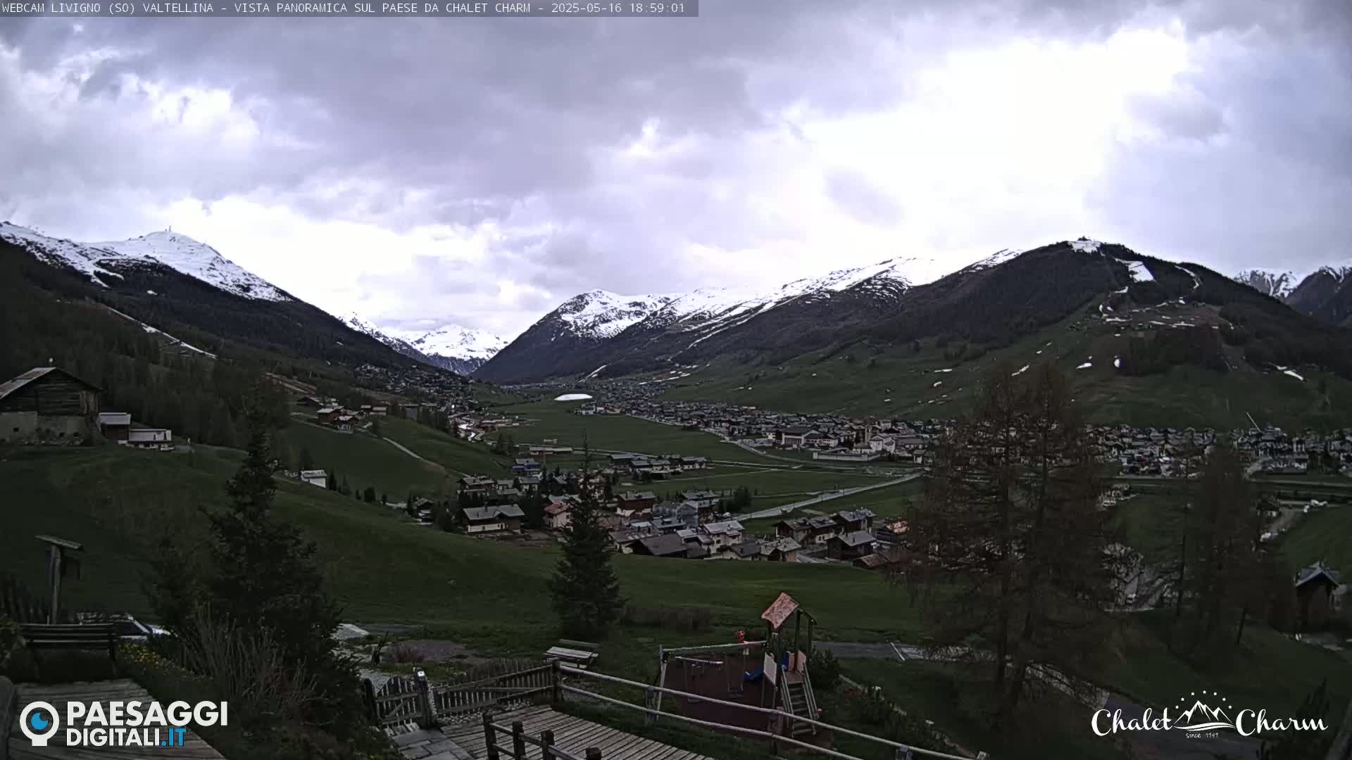 A panoramic view of a snow-capped mountain valley town under a partly cloudy sky.