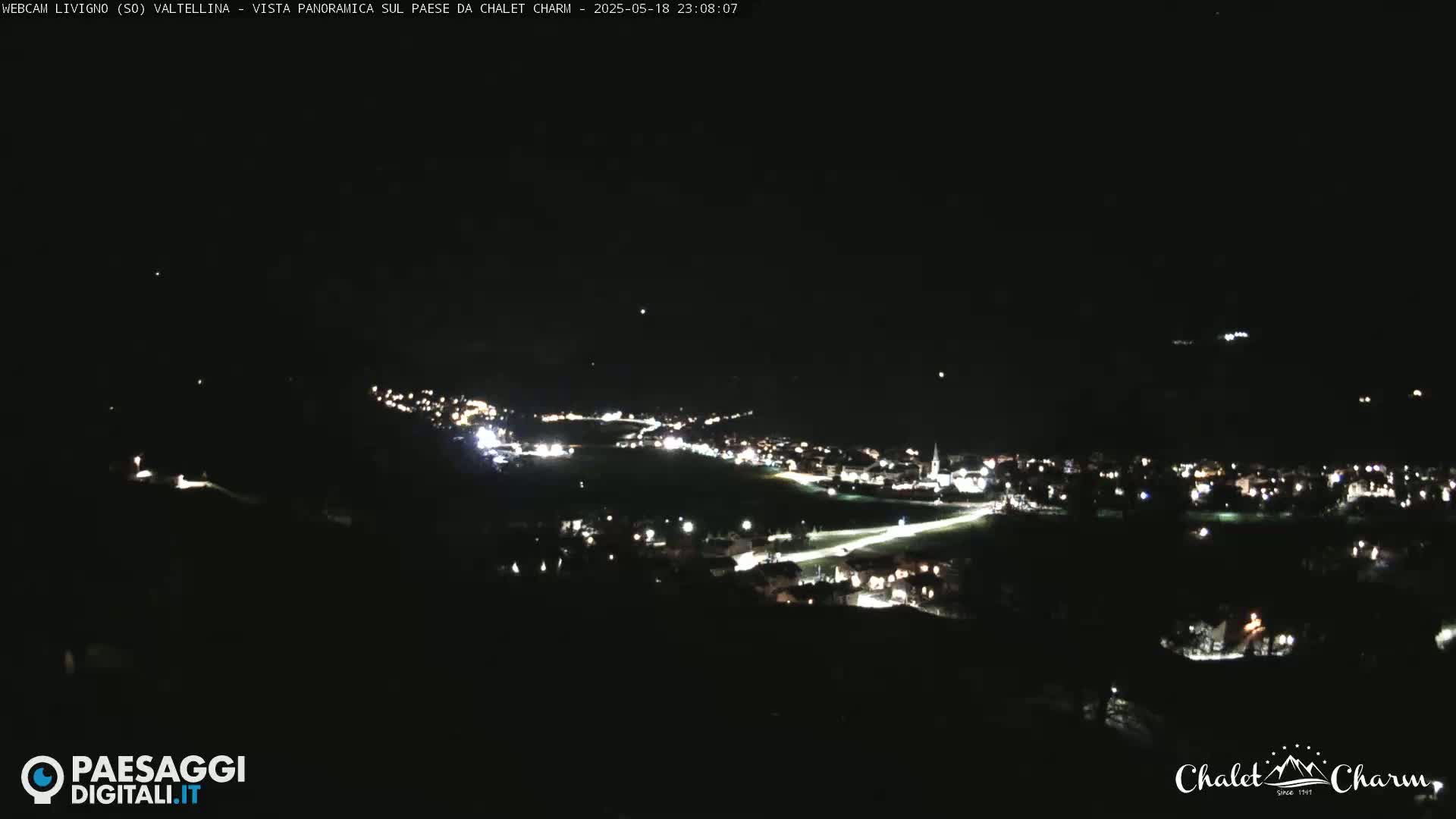 A nighttime, panoramic view of a town illuminated by lights, nestled in a dark valley under a clear sky.