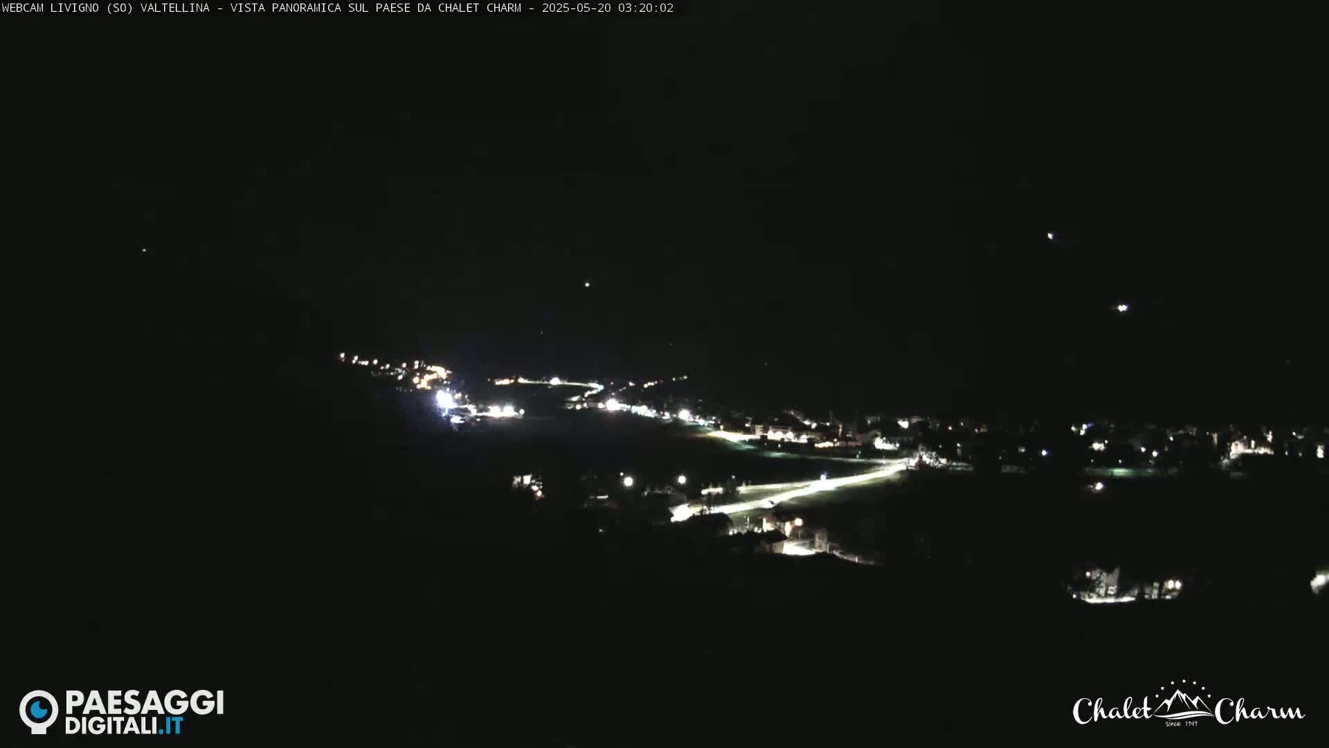 A nighttime panoramic view of a town illuminated by streetlights, under a clear, dark sky.