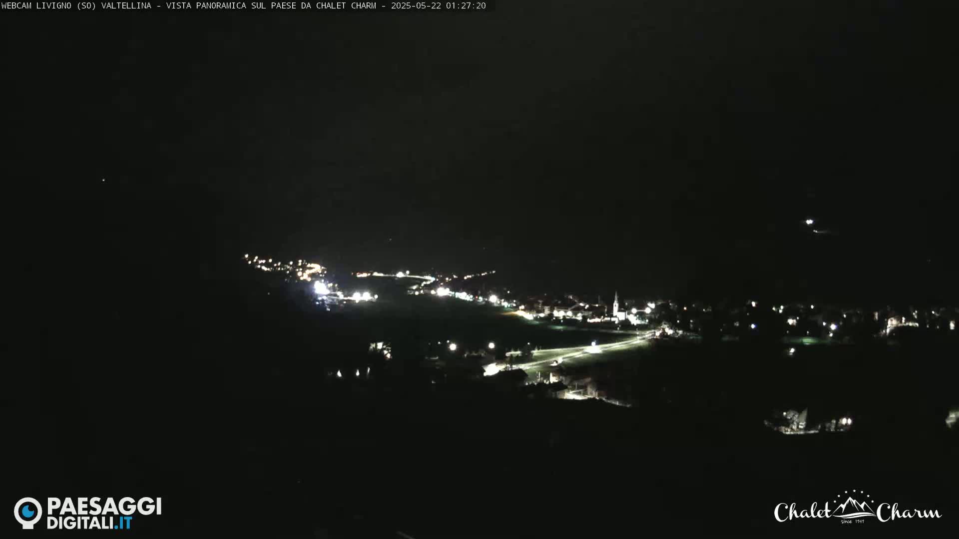 A nighttime, long-range view of a town's illuminated streets and buildings nestled in a dark landscape.