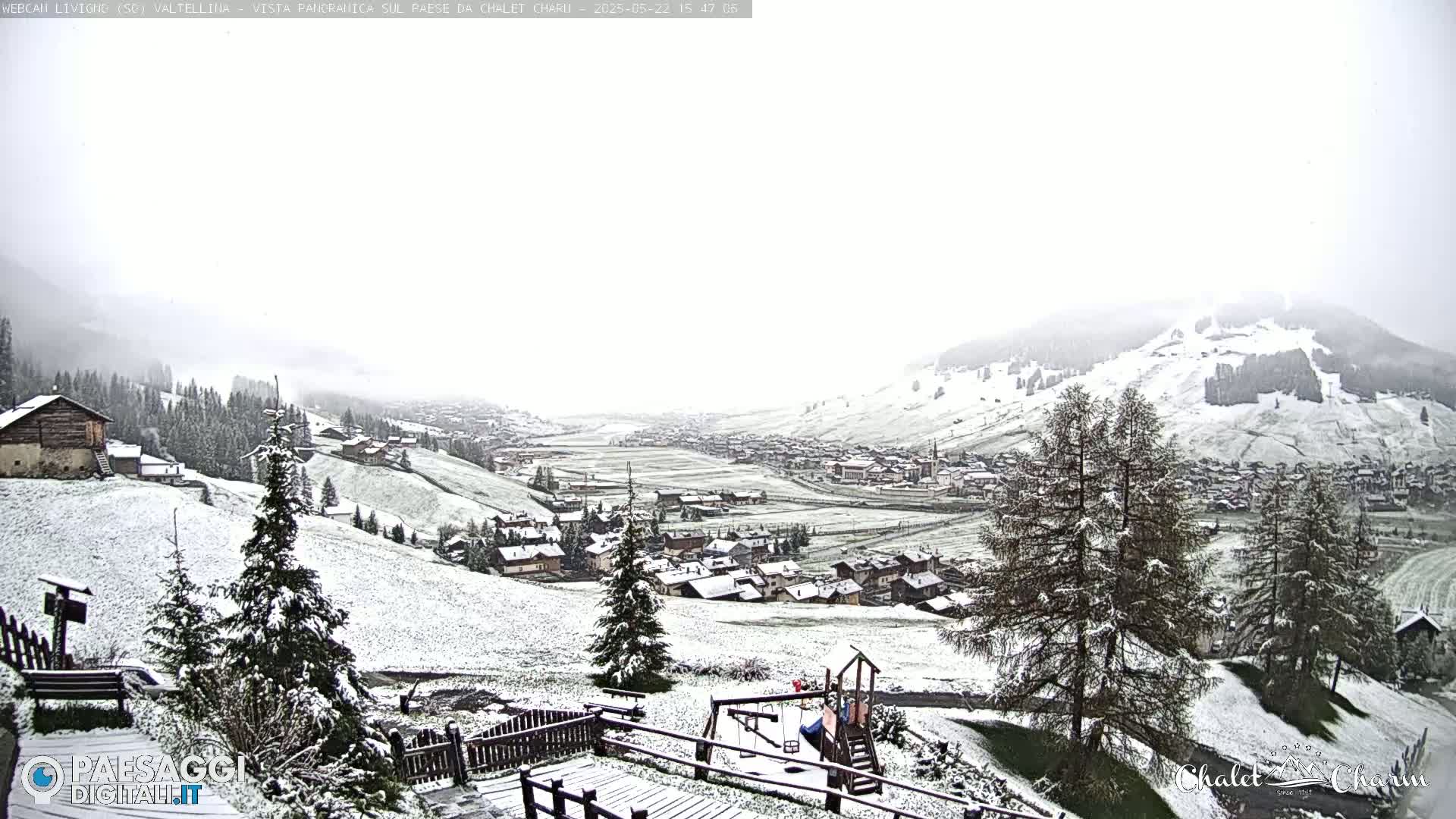 A snow-covered village nestled in a valley, with snow falling and mountains in the background.