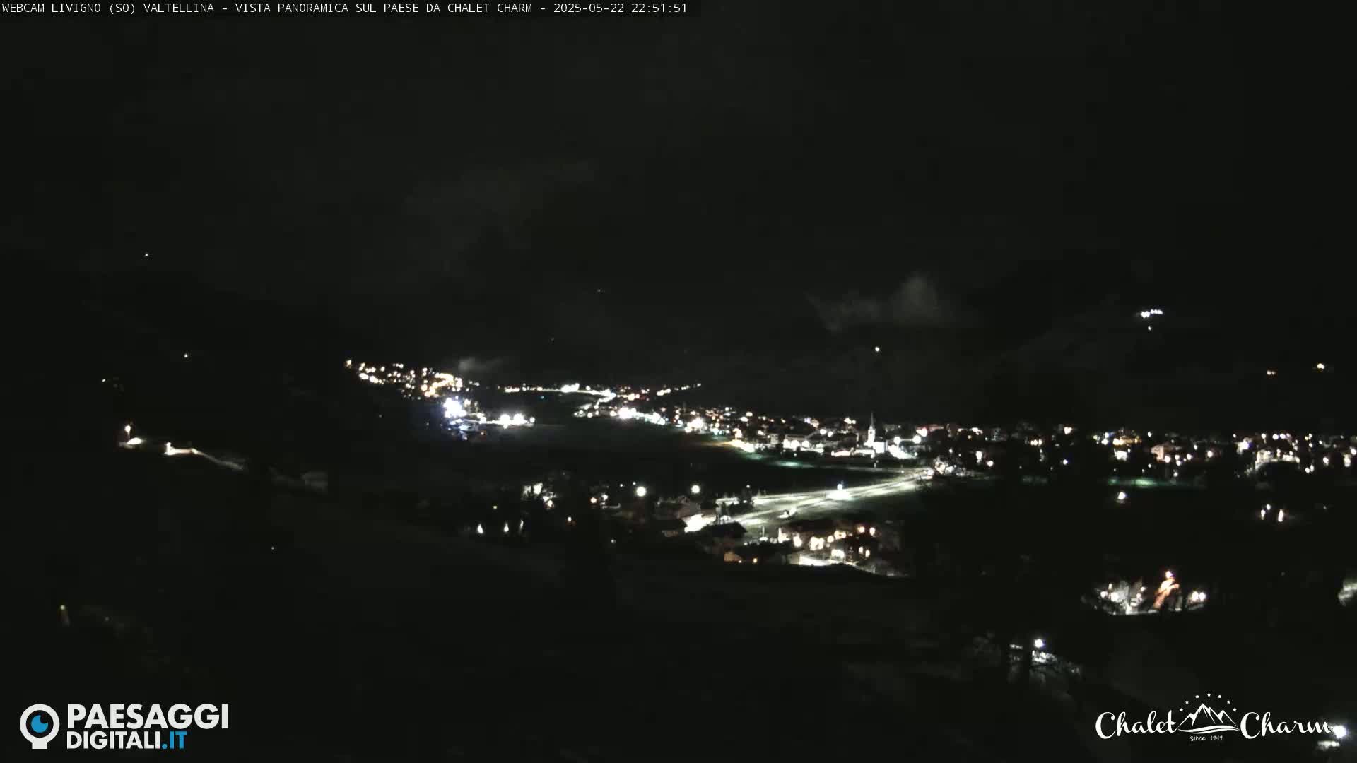 A nighttime, panoramic view of a small town illuminated by scattered lights, under a dark, mostly clear sky.