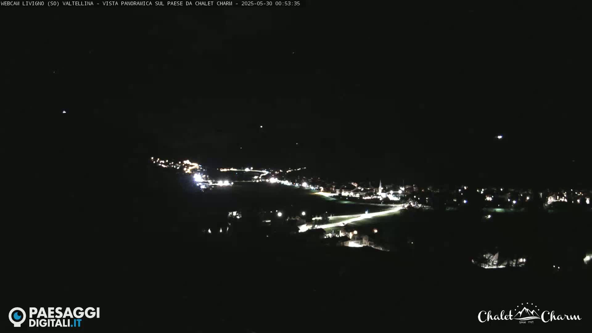 A nighttime panoramic view of a small town illuminated by streetlights under a clear, dark sky.