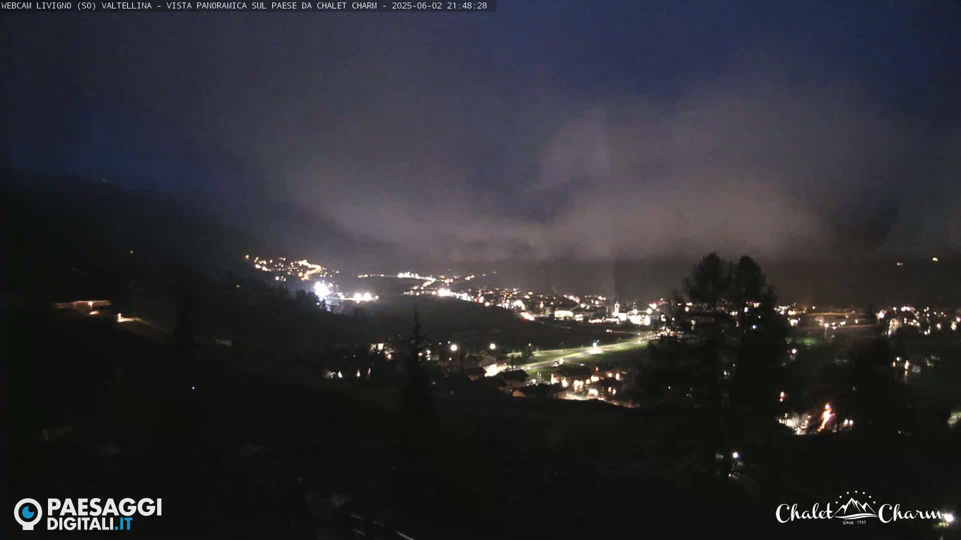 A nighttime panoramic view of a town nestled in a valley, shrouded in low-lying clouds or fog.