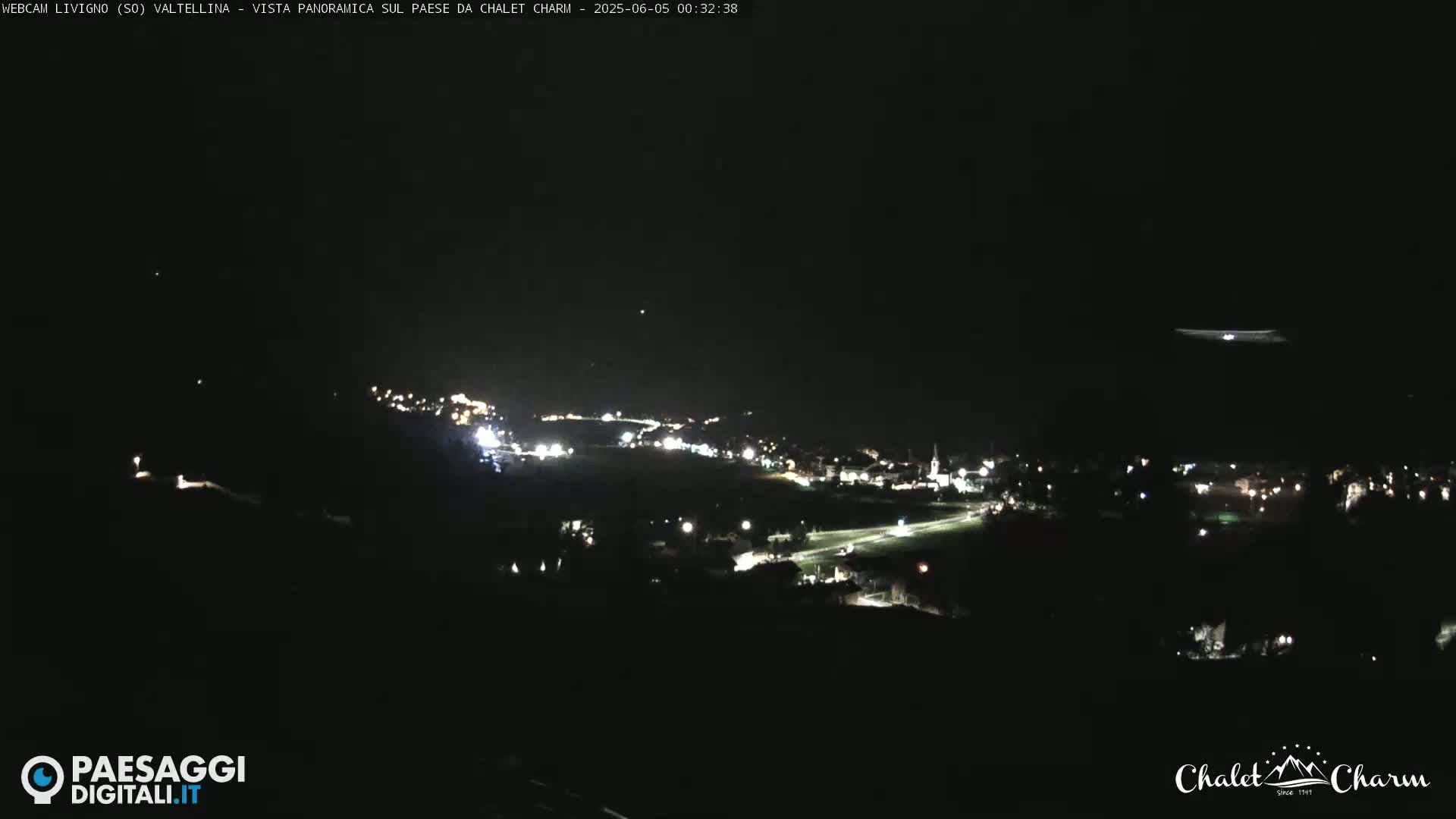 A nighttime, panoramic view of a small town illuminated by scattered lights under a dark, clear sky.
