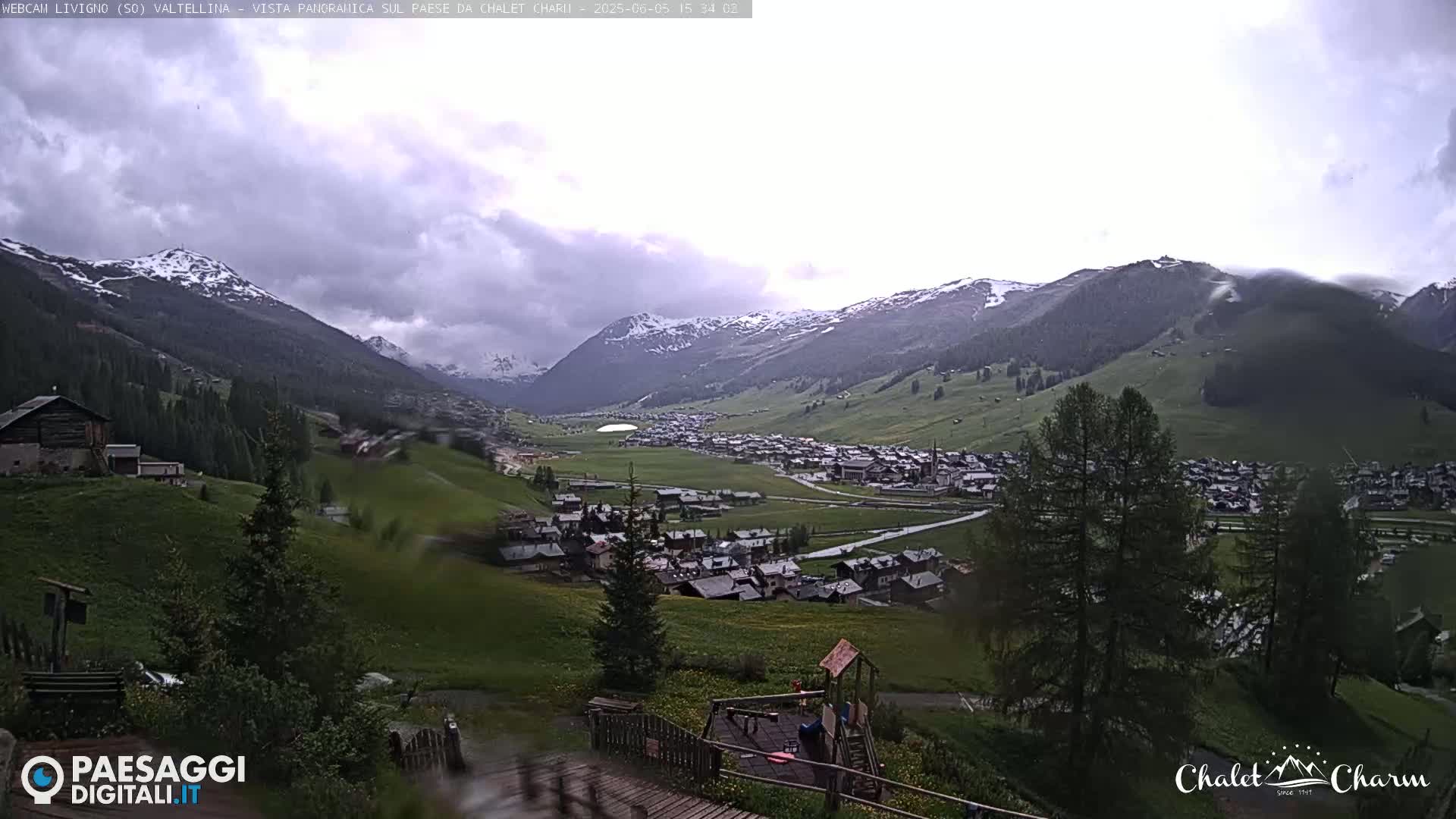 A rain-soaked view overlooks a valley town nestled between snow-capped mountains.