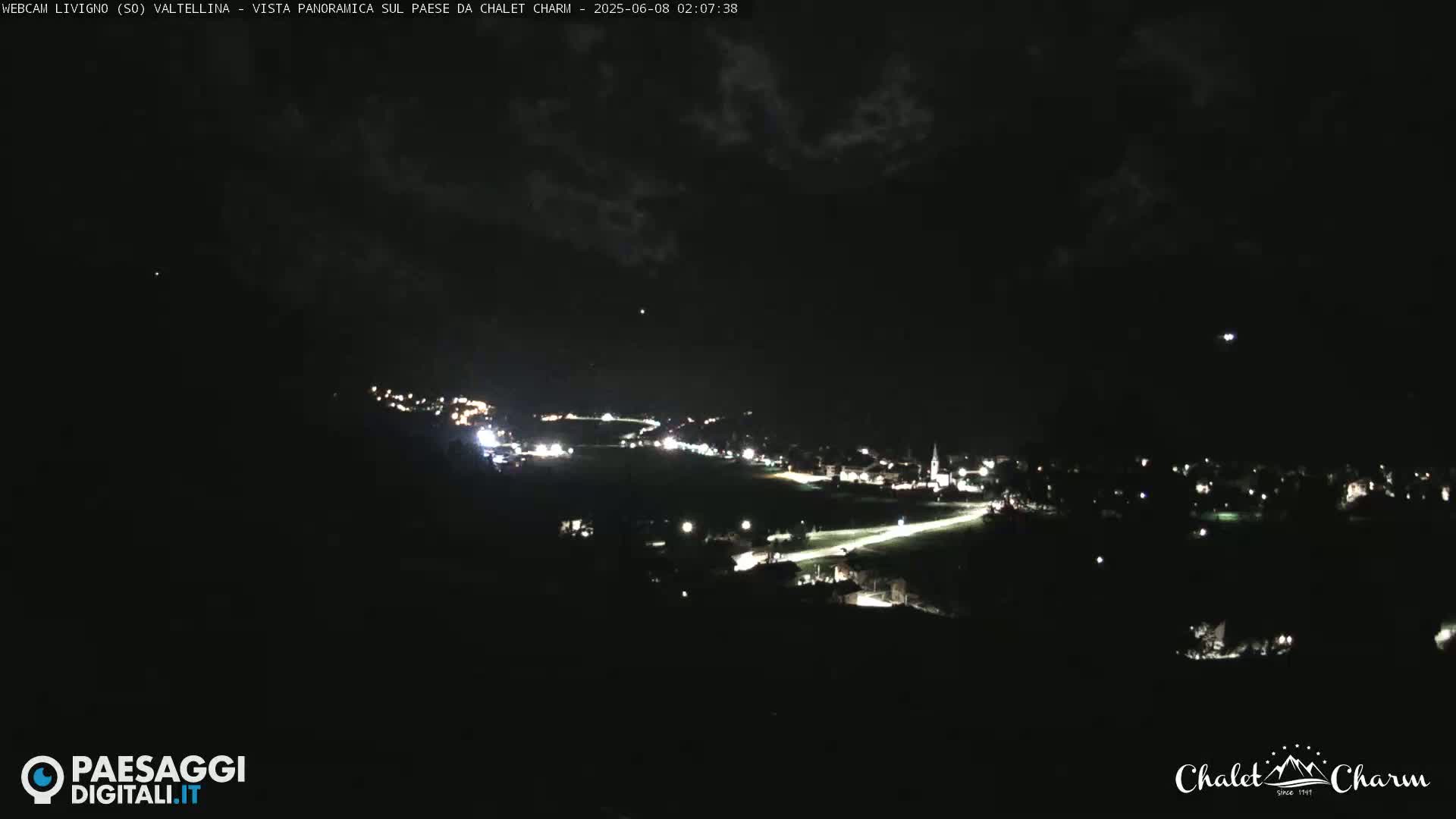 A nighttime long shot of a town with scattered lights under a mostly cloudy sky.
