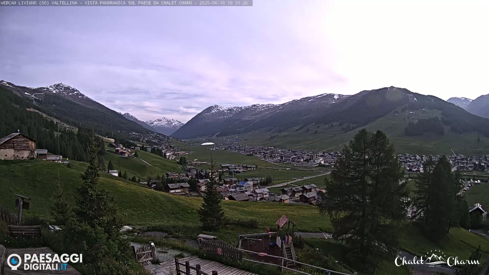 A panoramic view of a mountain village nestled in a valley under a partly cloudy twilight sky.