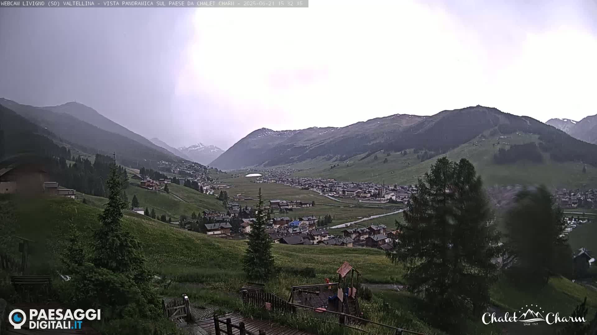 A panoramic view of a valley town nestled between mountains under an overcast sky.