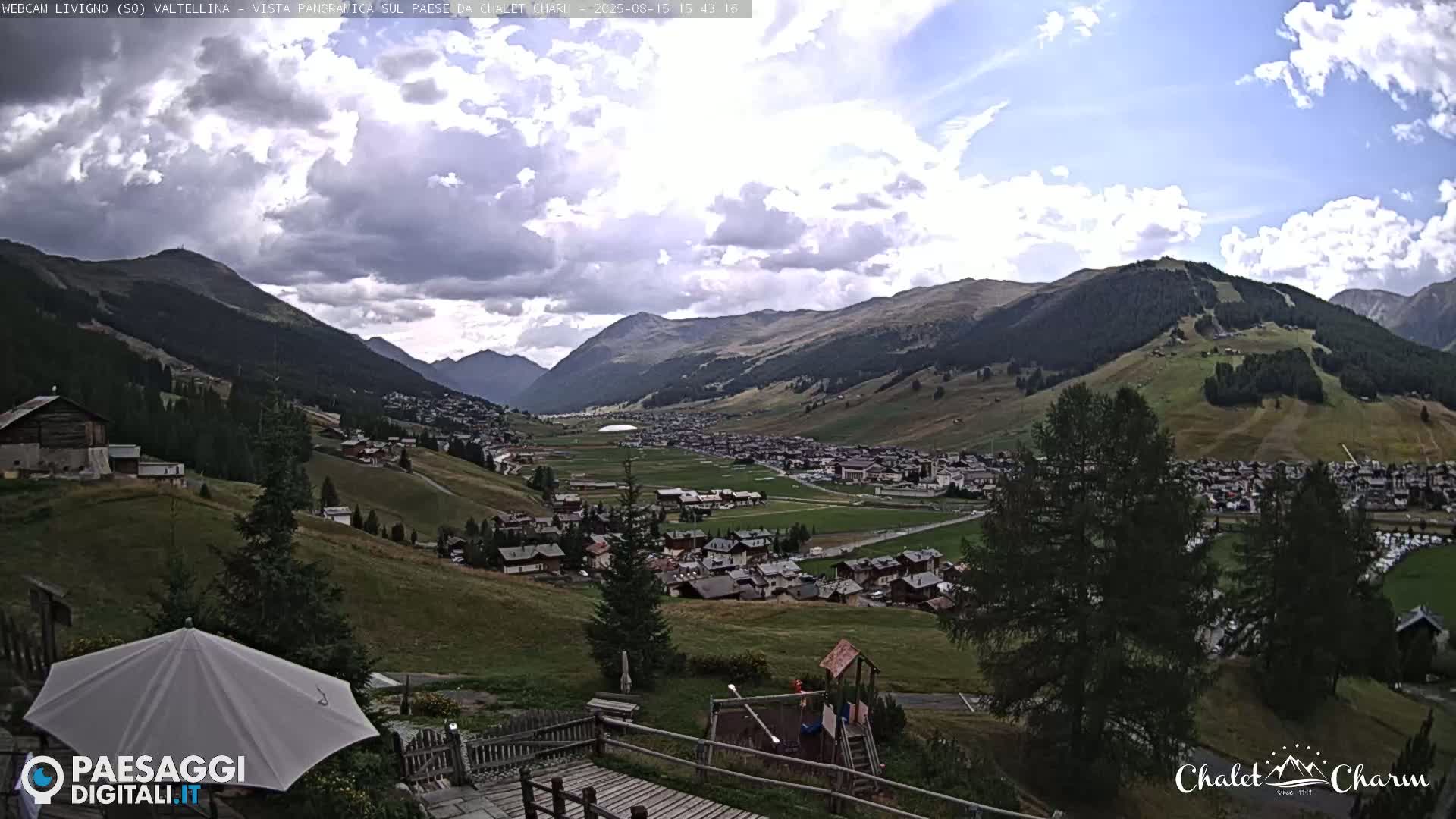 A panoramic view of a valley town nestled between mountains on a clear, sunny day, with a playground visible in the foreground.