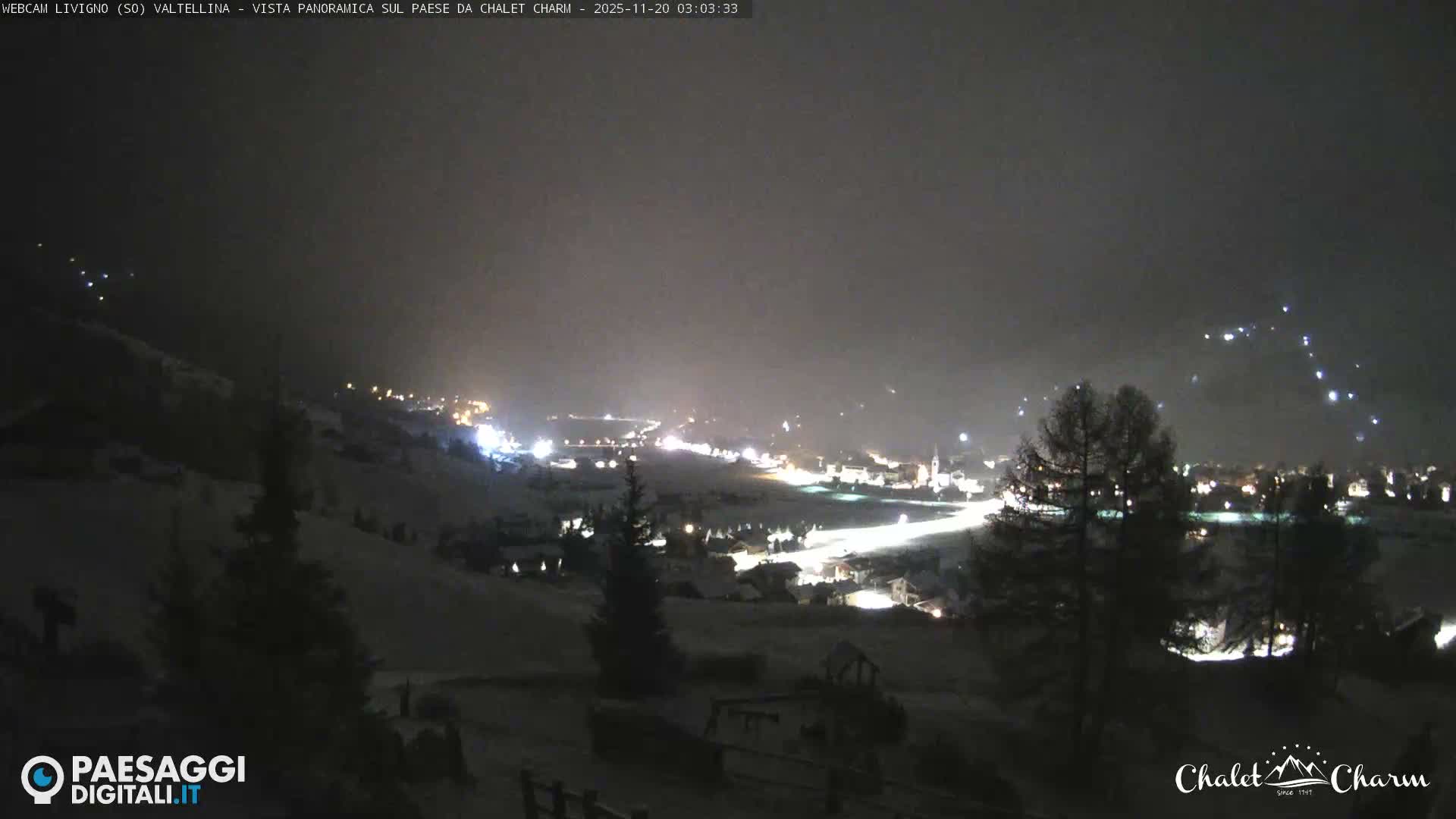 A snow-covered mountain village twinkles with numerous lights under a dark, hazy winter night sky.