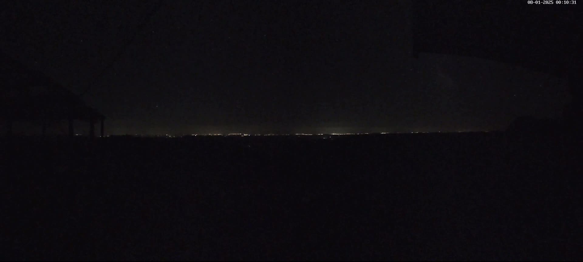 A nighttime view shows a distant city's lights on the horizon under a clear, dark sky.