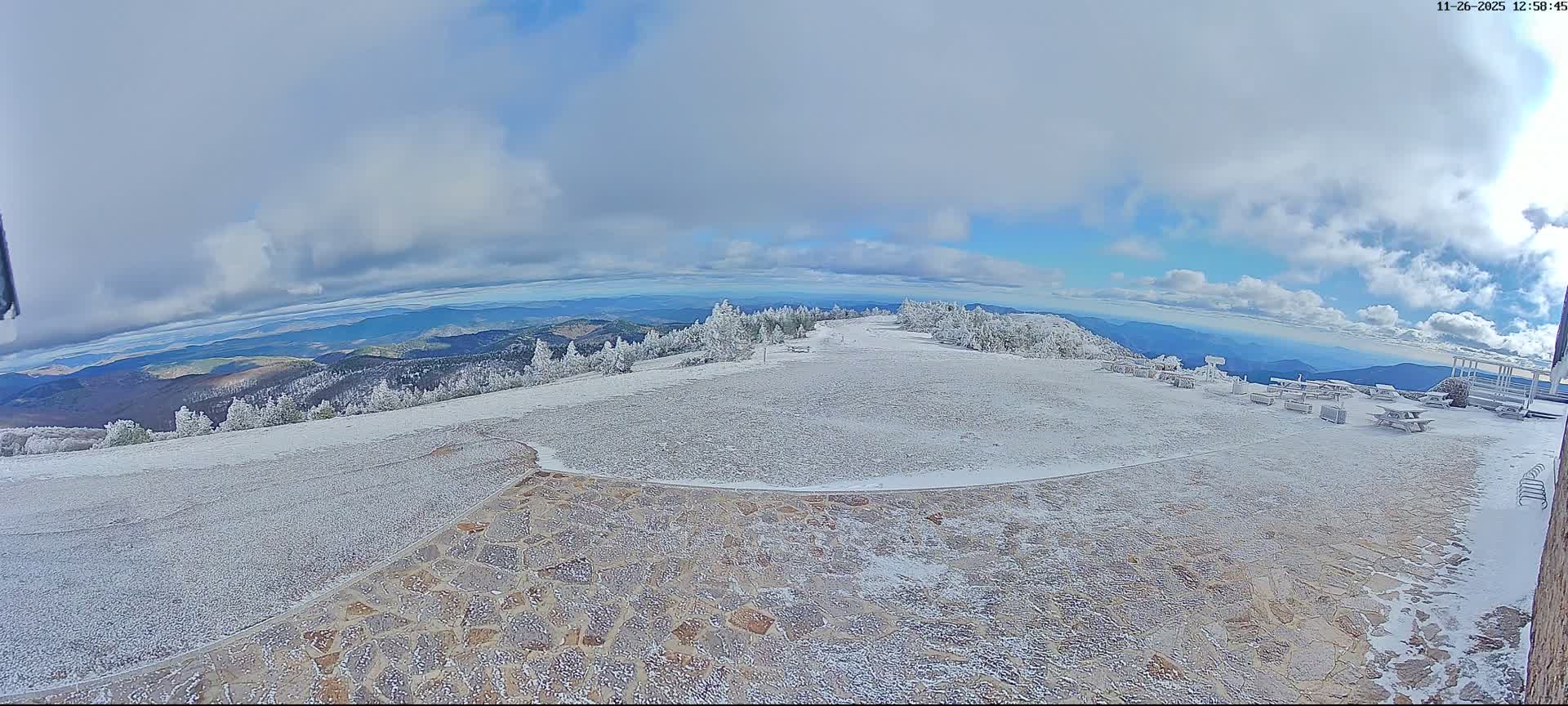 A dense fog envelops a damp, rocky observation area with picnic tables and a few scattered trees, creating a hazy, overcast day.