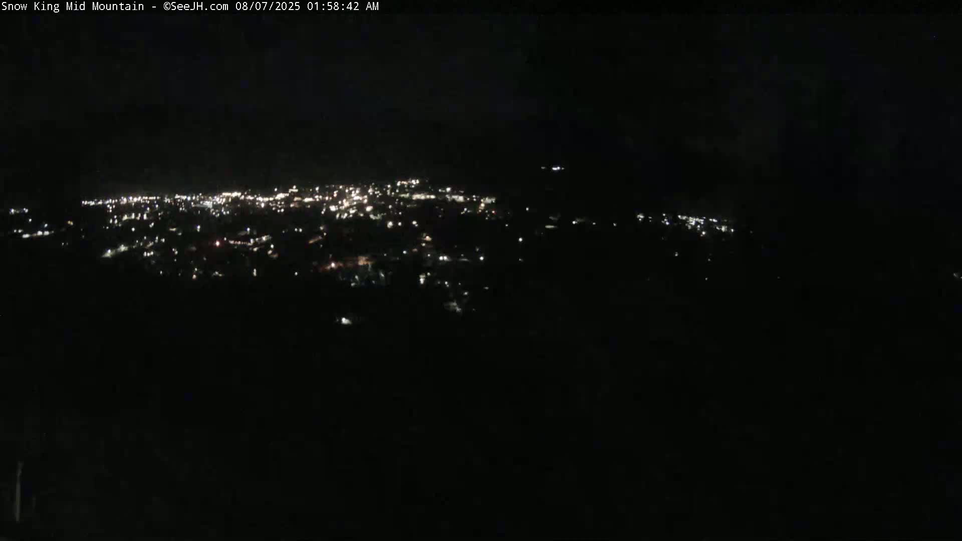A nighttime, high-angle view shows a city's lights spread across a dark landscape.