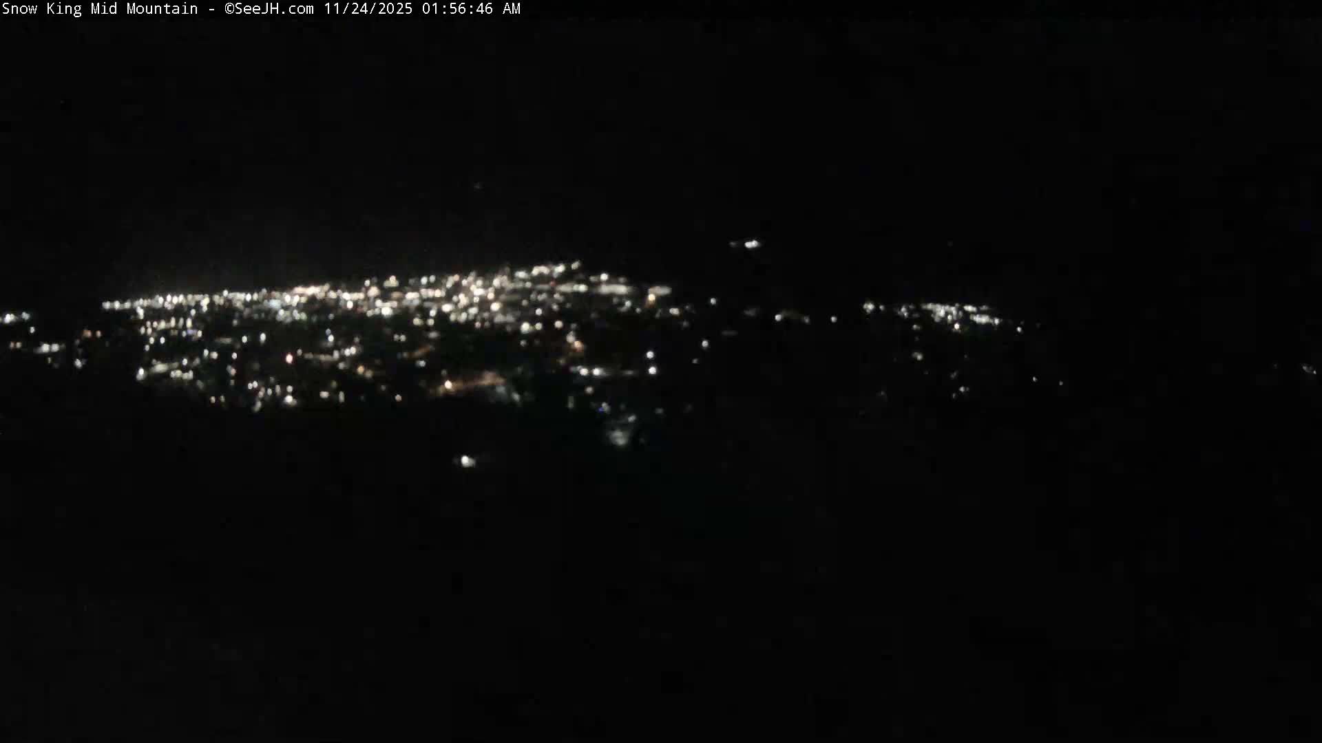 A panoramic, blurry view of a distant town's lights illuminates the dark landscape at night under clear conditions.