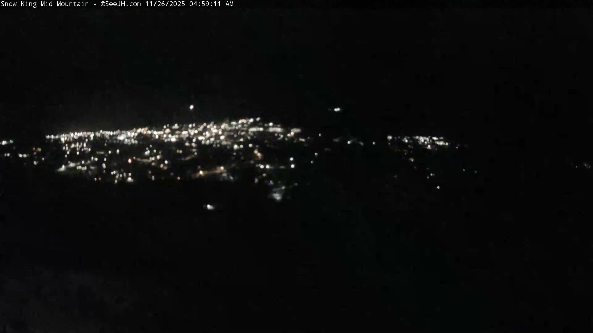 A panoramic, blurry view of a distant town's lights illuminates the dark landscape at night under clear conditions.