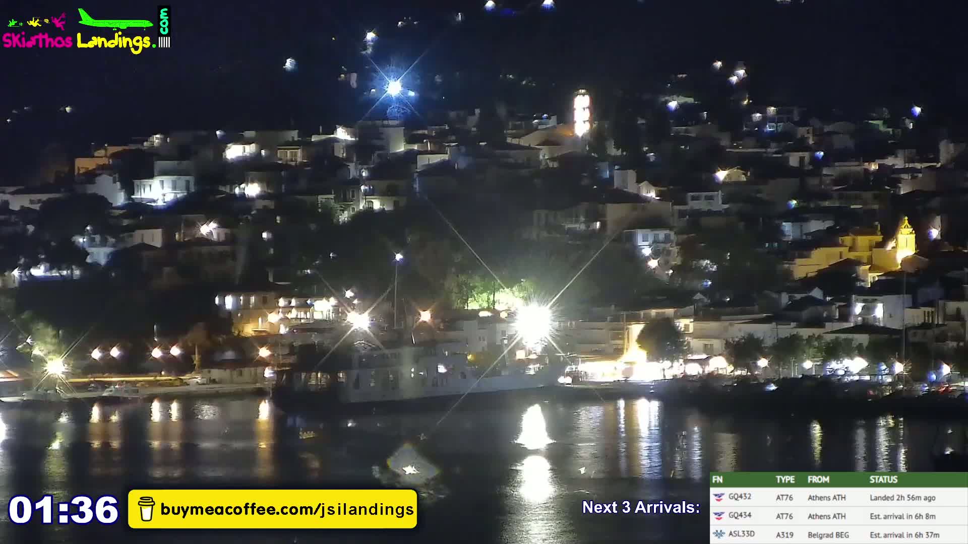 A nighttime view of a town's waterfront illuminated by lights, reflecting on calm water.