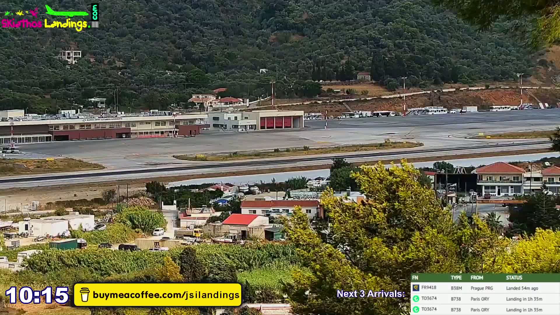 A long shot of an airport terminal, runway, and surrounding landscape on a clear day, with hills visible in the background.