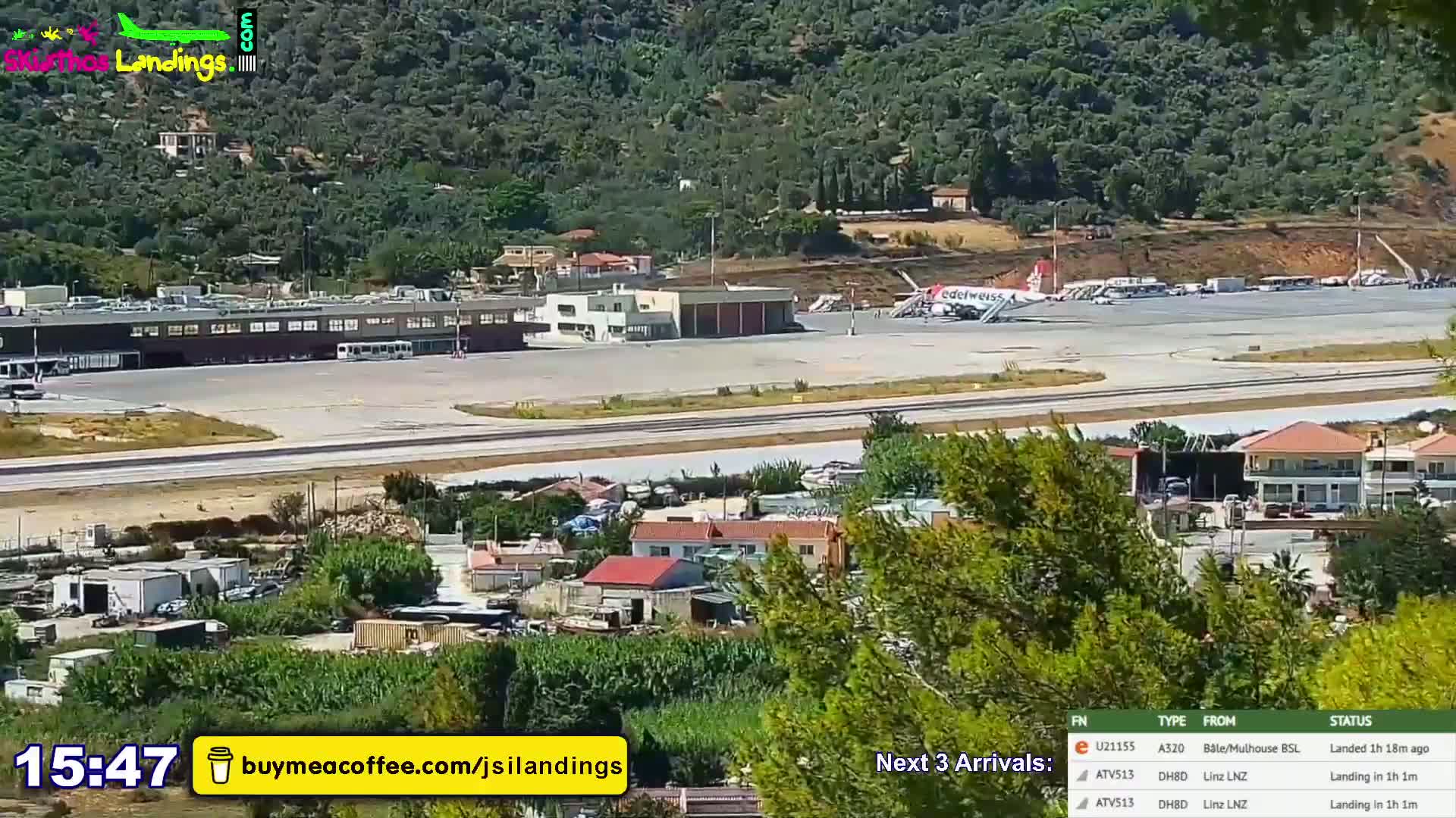 A long shot of an airport terminal, runway, and surrounding landscape on a clear day, with hills visible in the background.