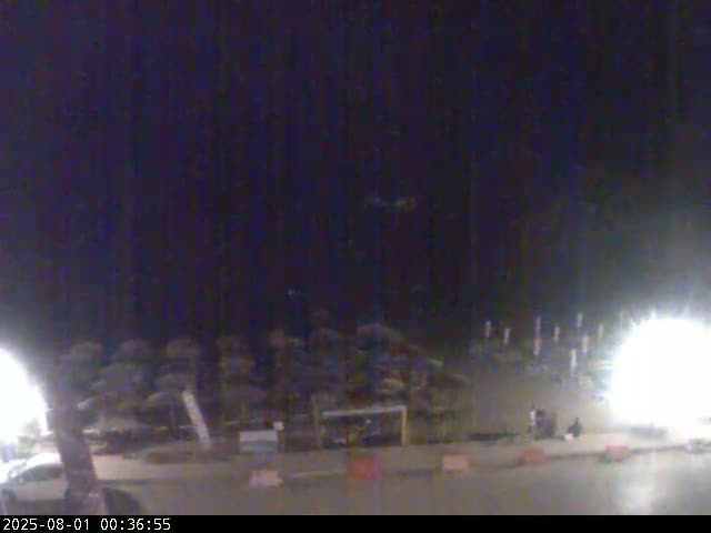 A nighttime view of a beach with umbrellas and some people present, under a dark sky.