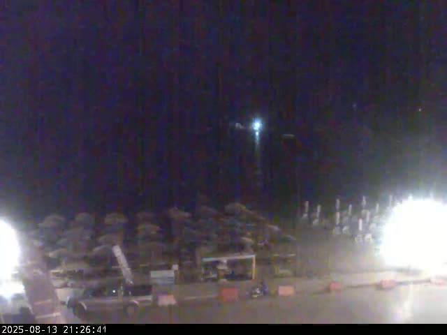 A nighttime view of a beach with closed umbrellas and bright fireworks displays in the distance.