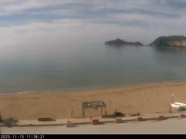 A wide sandy beach meets a calm sea with distant islands under a partly cloudy sky.