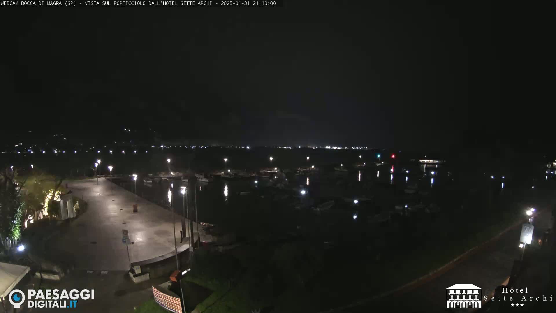 A nighttime view of a harbor filled with boats, illuminated by lights along a paved waterfront.