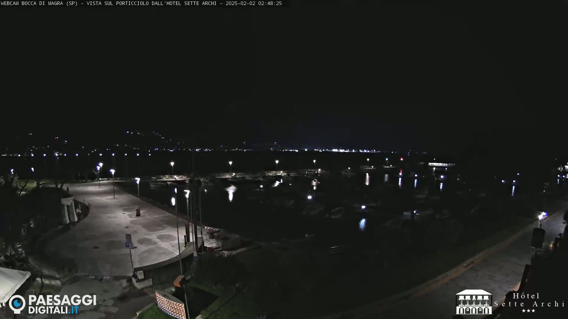 A nighttime view of a harbor filled with boats, illuminated by lights along a paved waterfront area.