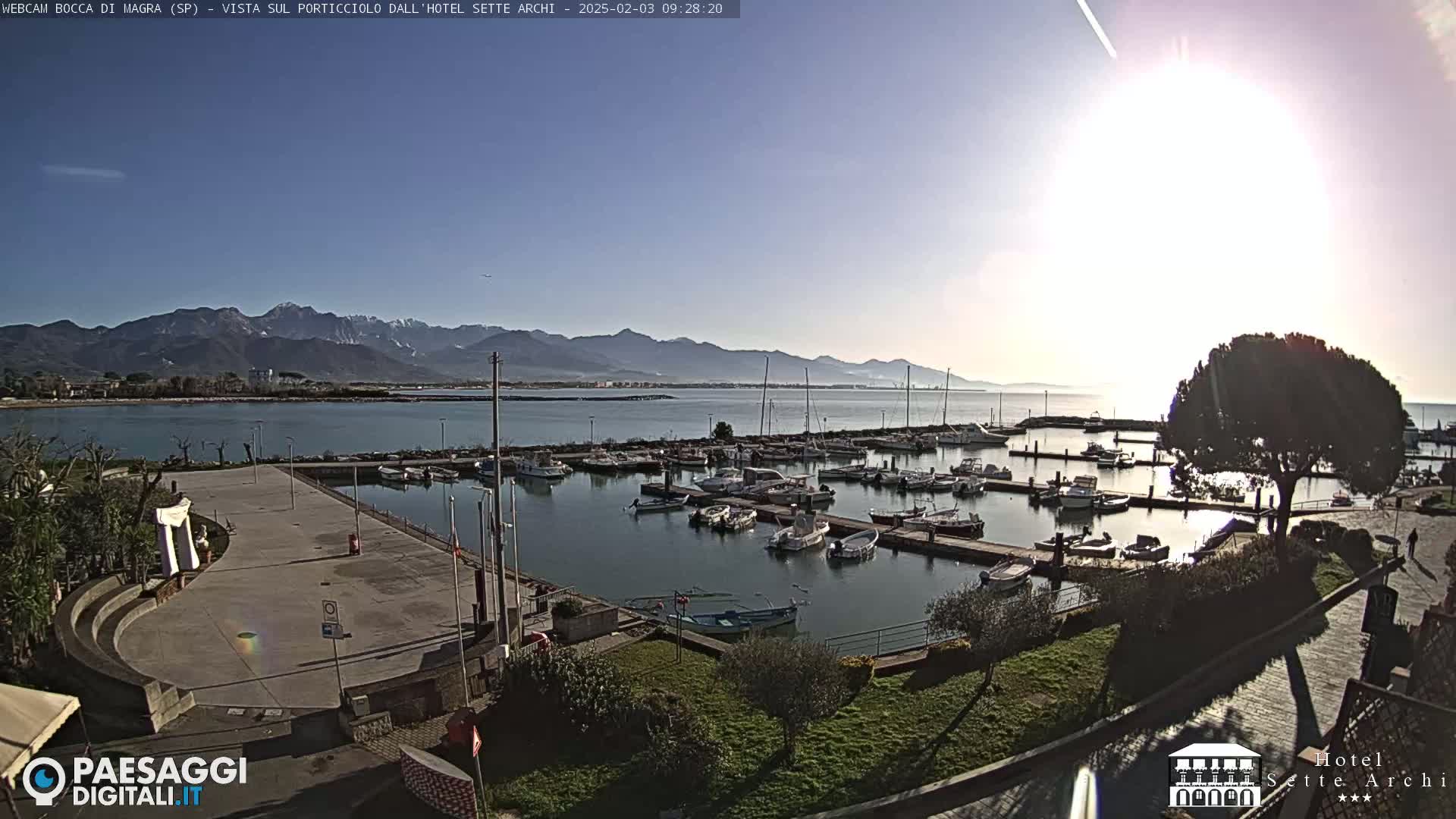 A sunny day overlooking a marina filled with boats, a paved plaza, and mountains in the distance.