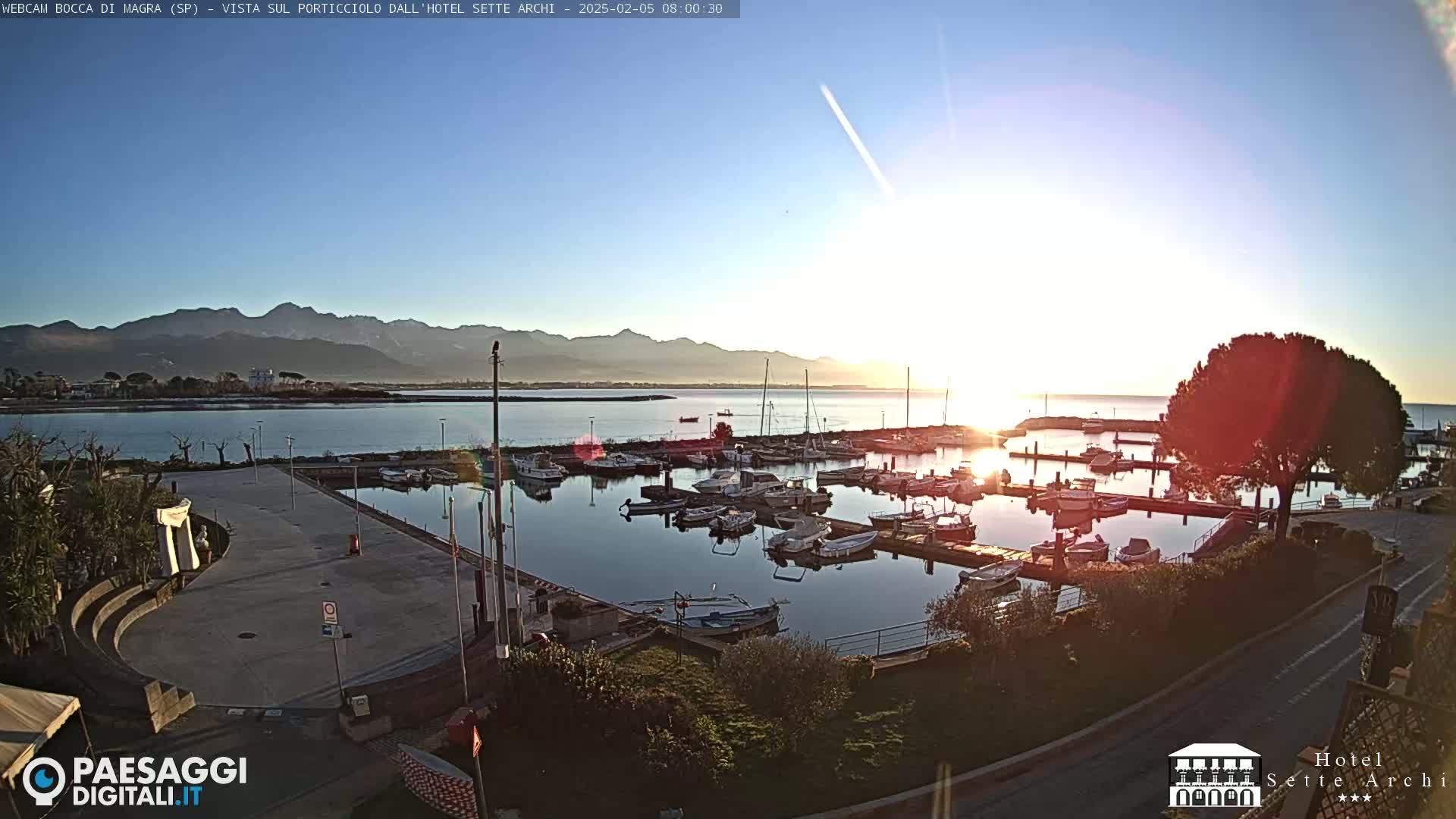 A marina filled with boats at sunrise, under a clear sky, with mountains in the distance.