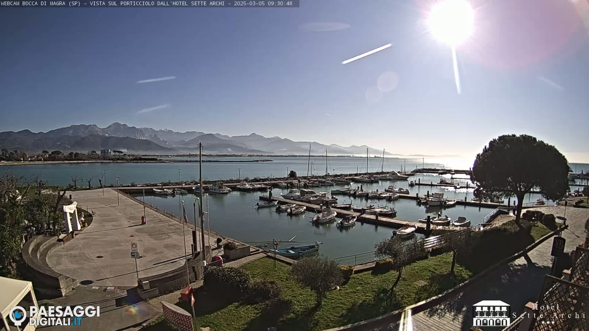 A sunny day overlooking a harbor filled with boats, a paved area, and mountains in the distance.