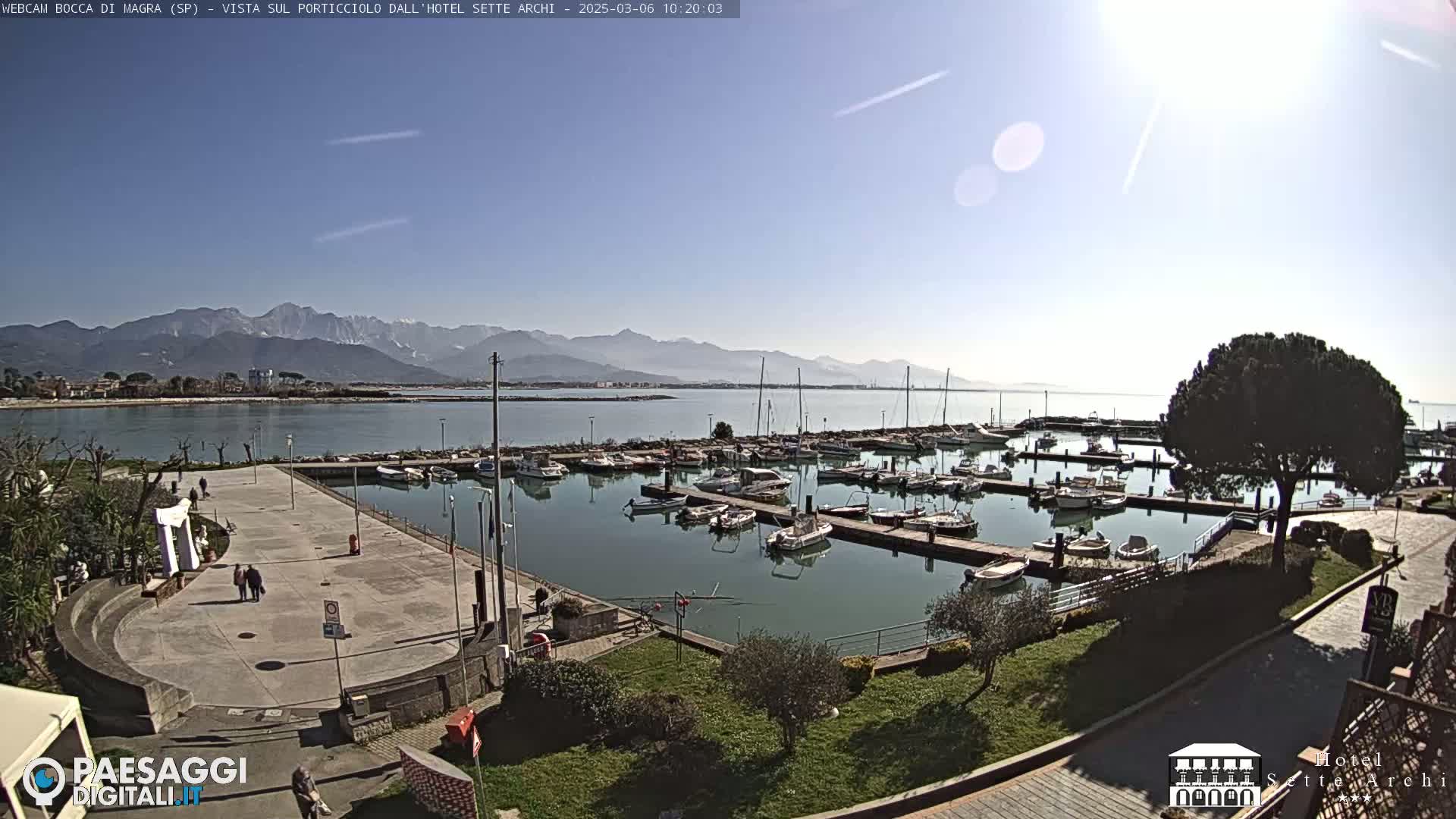 A marina filled with numerous boats is shown on a sunny day, with mountains in the distance.