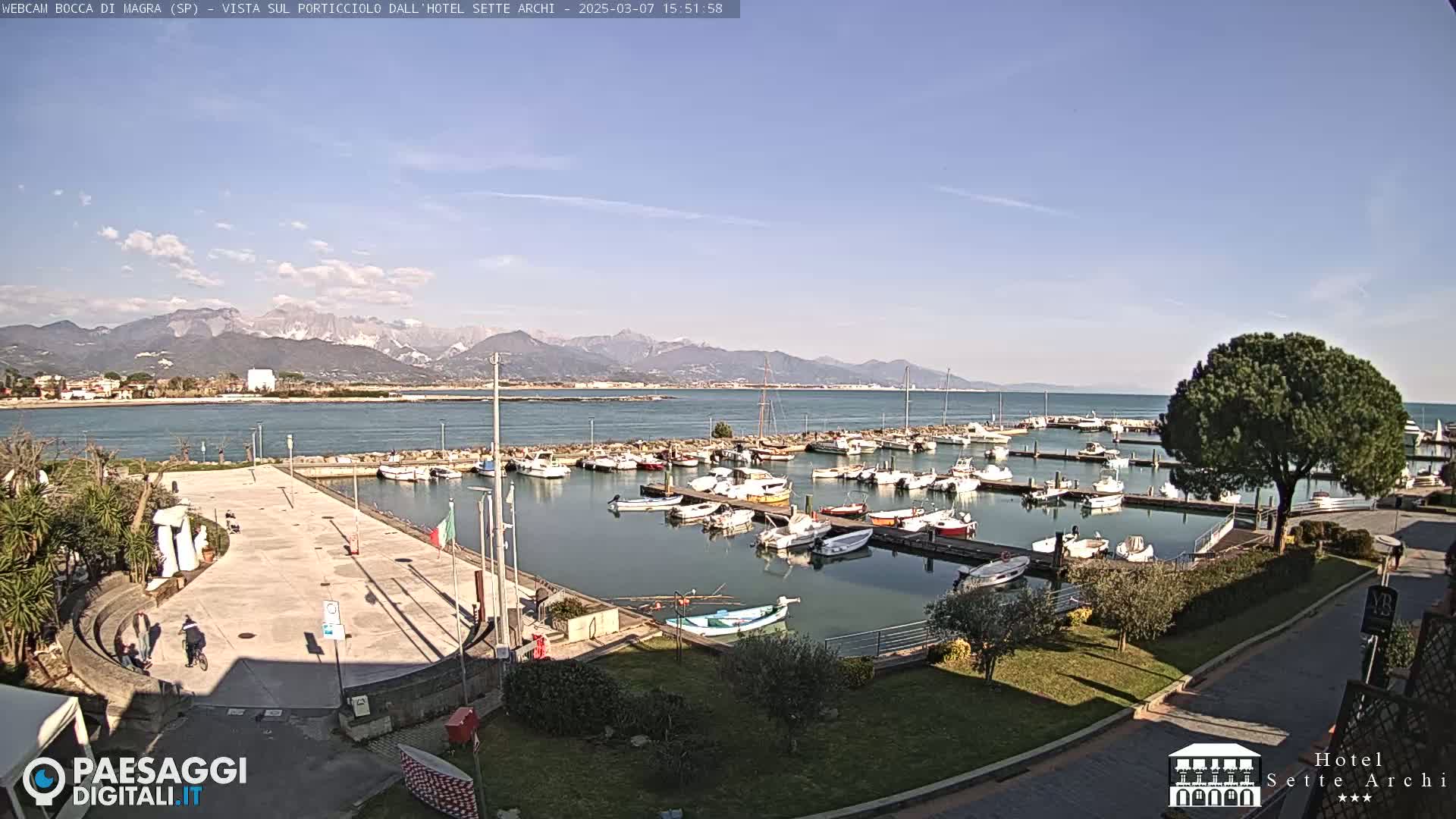A sunny day overlooking a harbor filled with boats, a paved area, and mountains in the distance.