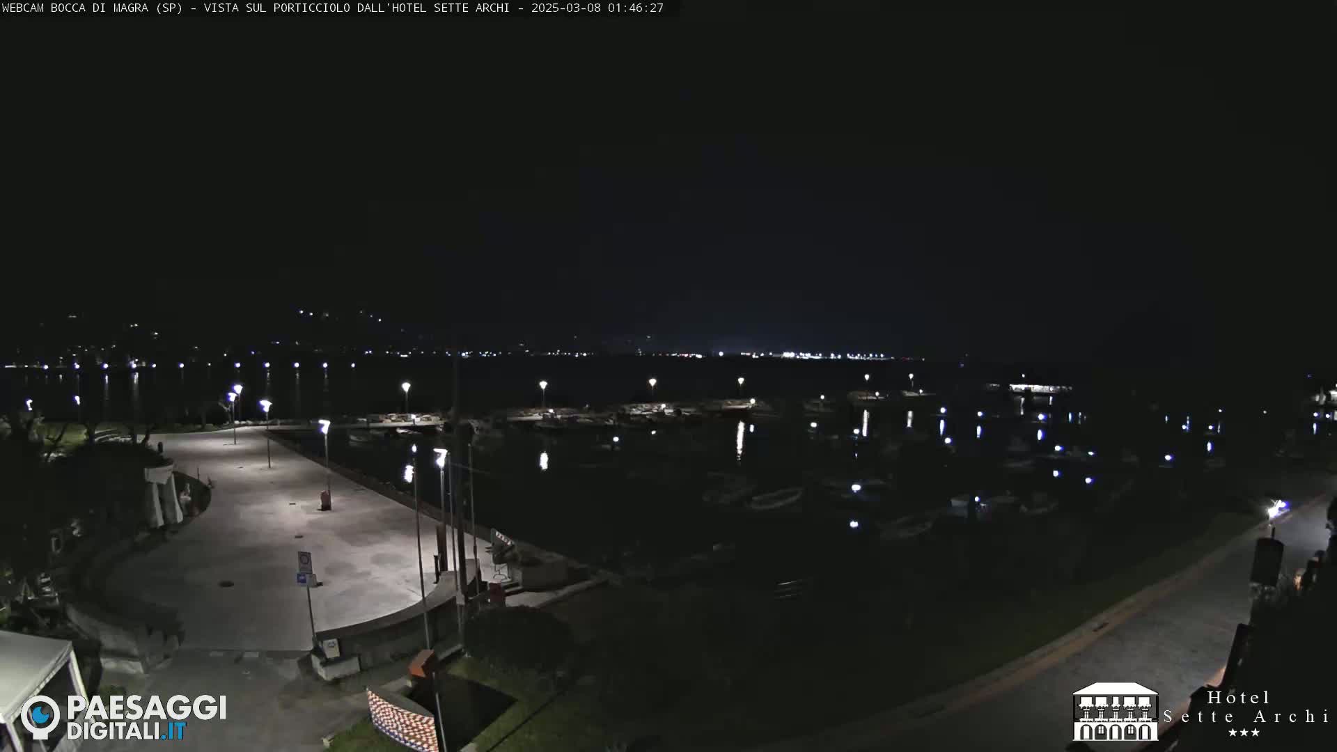 A nighttime view of a harbor filled with boats, illuminated by lights along a paved walkway.