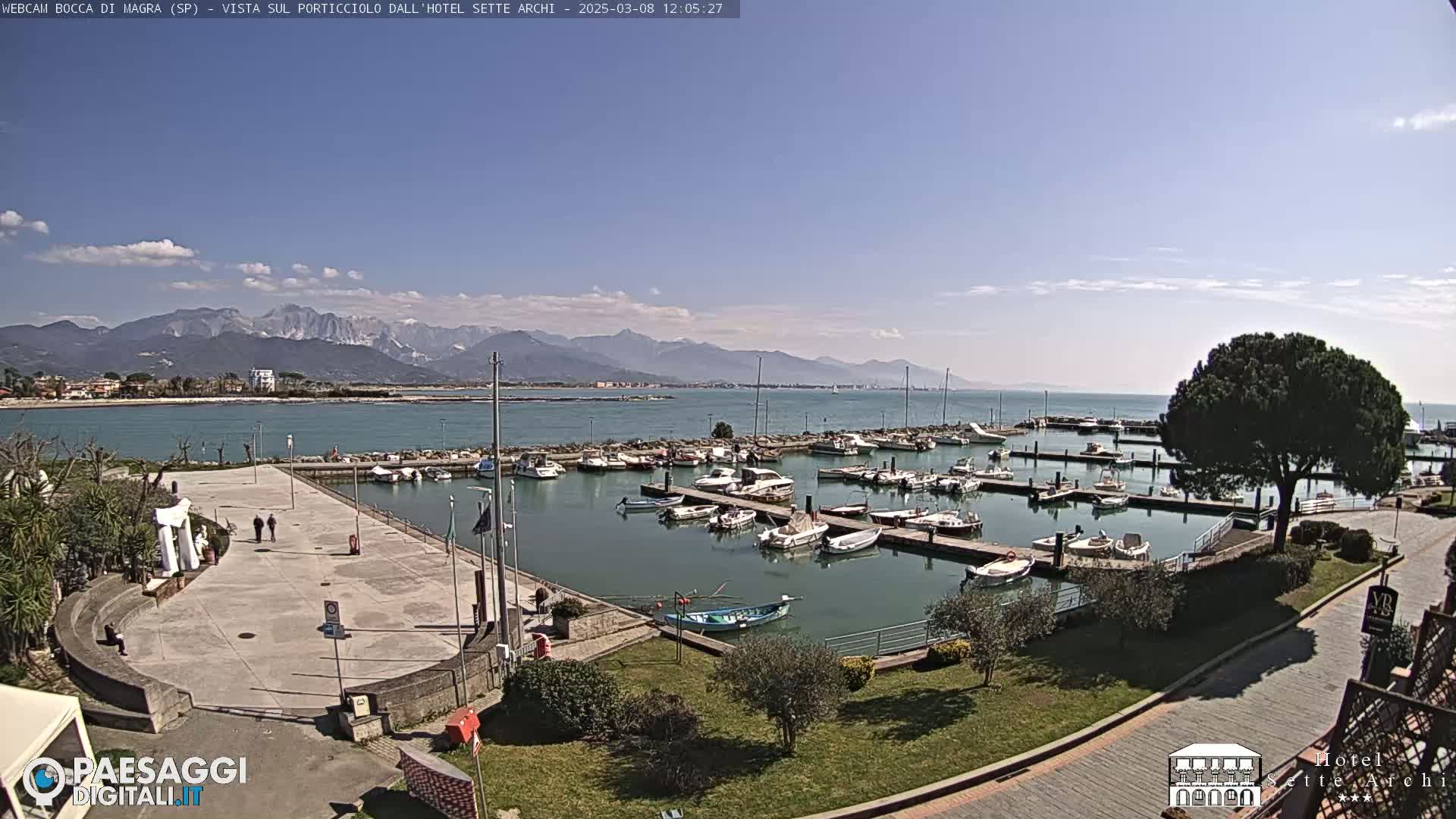 A sunny day overlooking a harbor filled with boats, a paved plaza, and distant mountains.