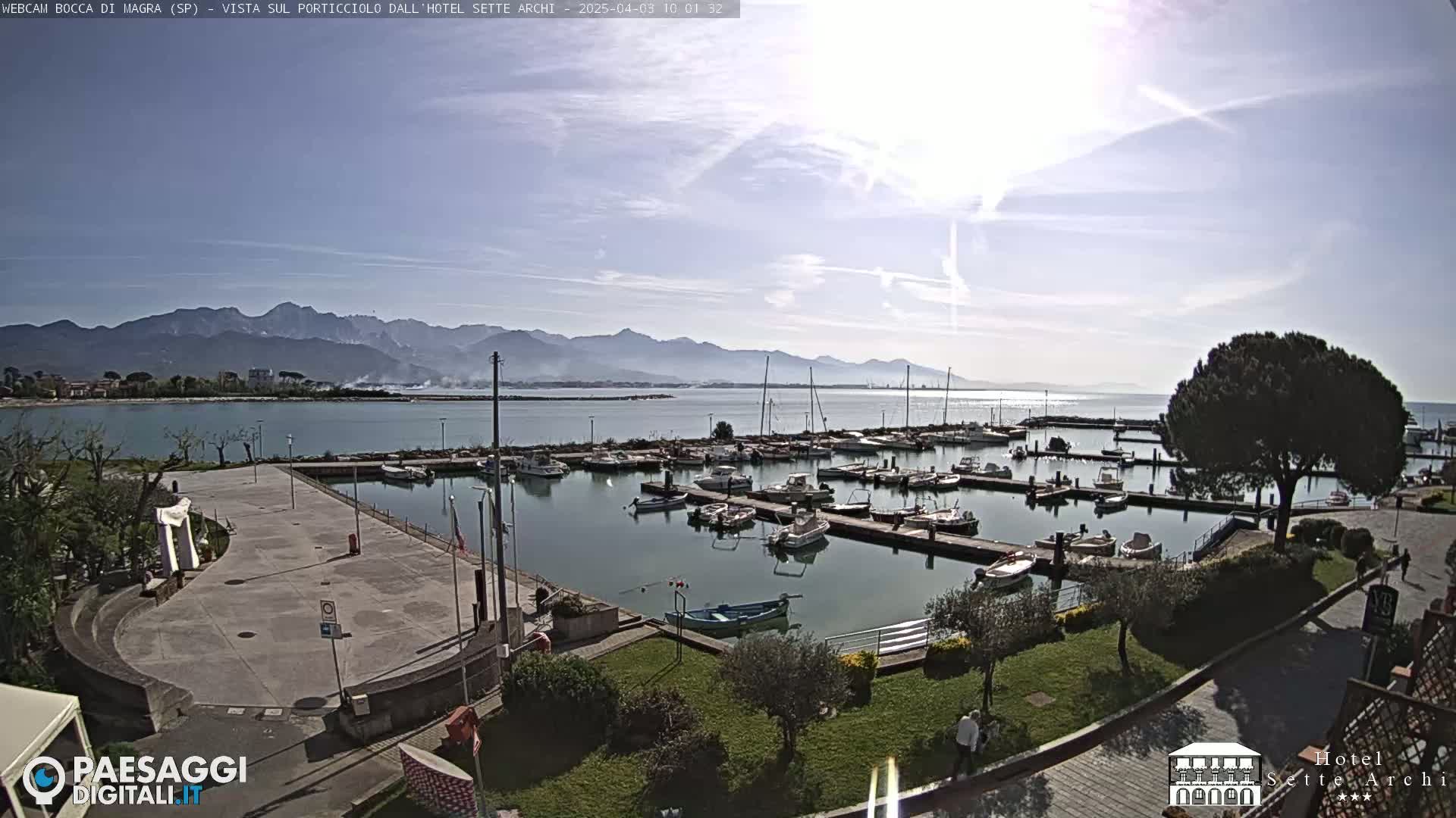 A sunny day overlooking a marina filled with boats, a paved plaza, and mountains in the distance.
