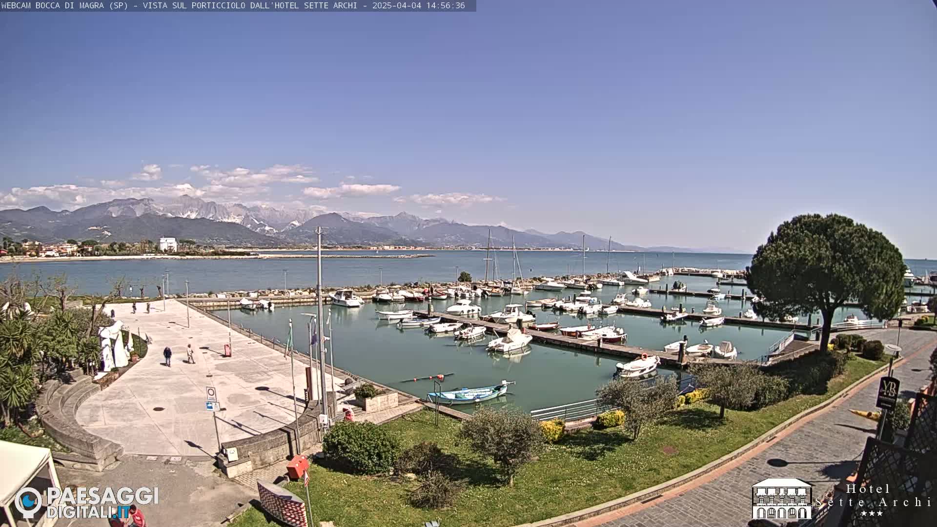 A marina filled with boats is shown on a sunny day with mountains in the background.